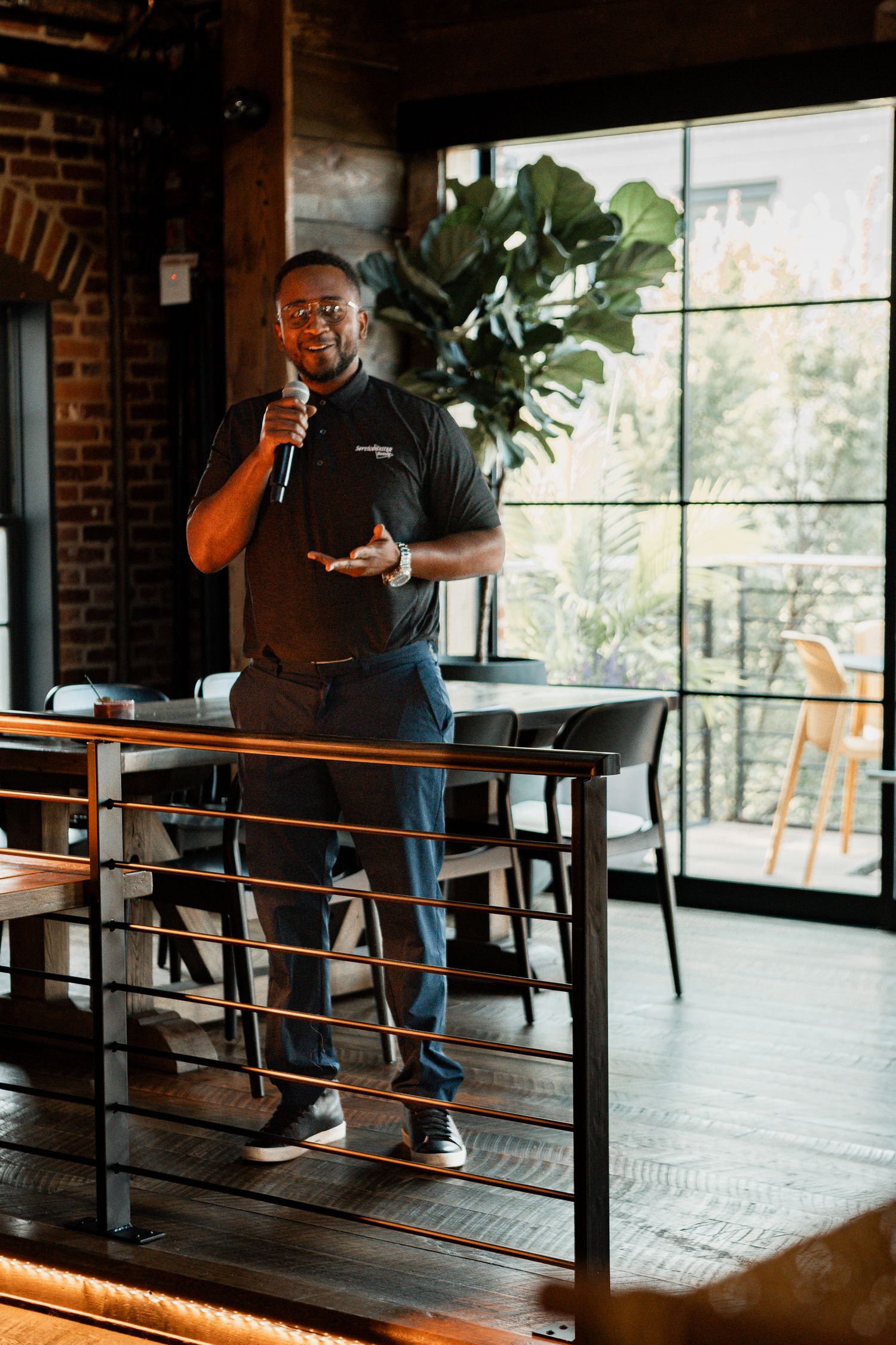 A person speaking at a podium in an industrial-style venue with brick walls and large windows.