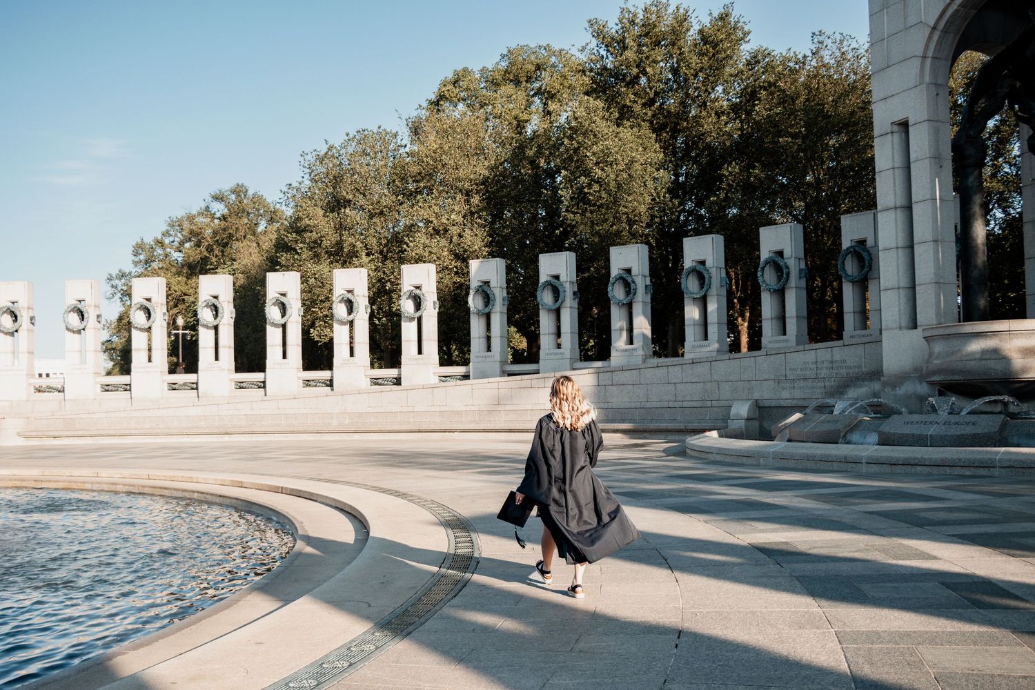 Person stands beneath majestic marble columns at Memorial Amphitheater in Arlington National Cemetery during sunset.