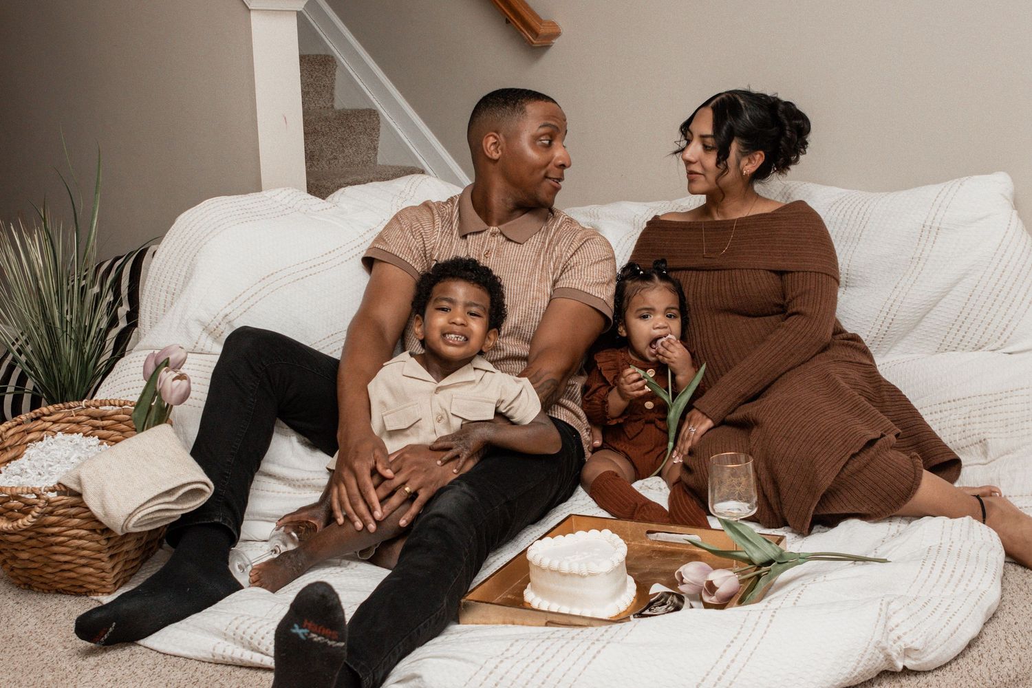 Family lounging together on white couch wearing coordinated brown and black outfits in intimate lifestyle photoshoot.