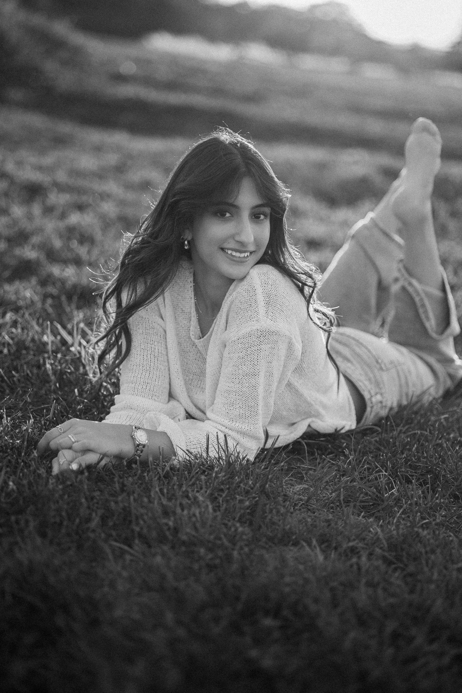 Black and white portrait of someone lying in grass wearing a cozy sweater, with a dreamy outdoor atmosphere.