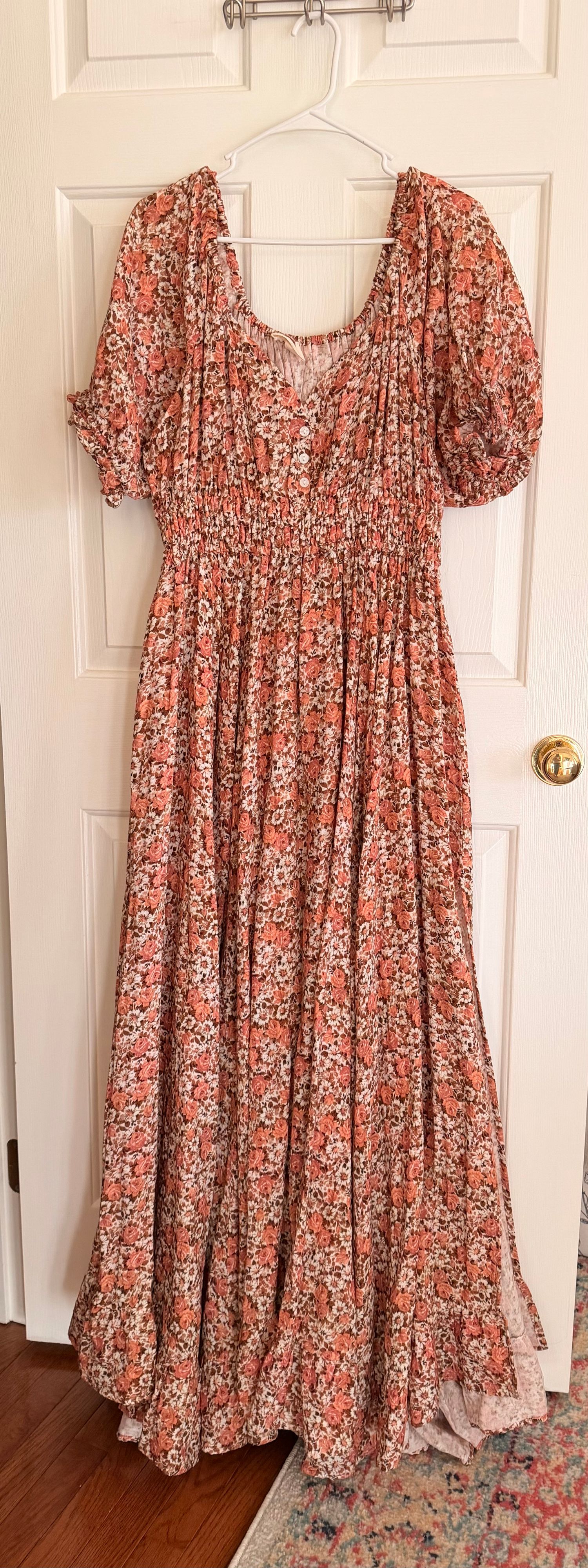 A floral print maxi dress with puff sleeves and smocked bodice shown hanging against a white door in multiple angles.