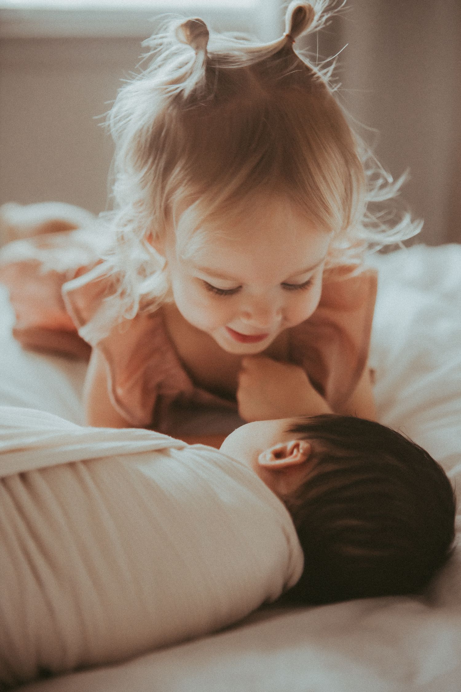Soft sepia-toned photo series showing a small child laying on white bedding in gentle morning light.