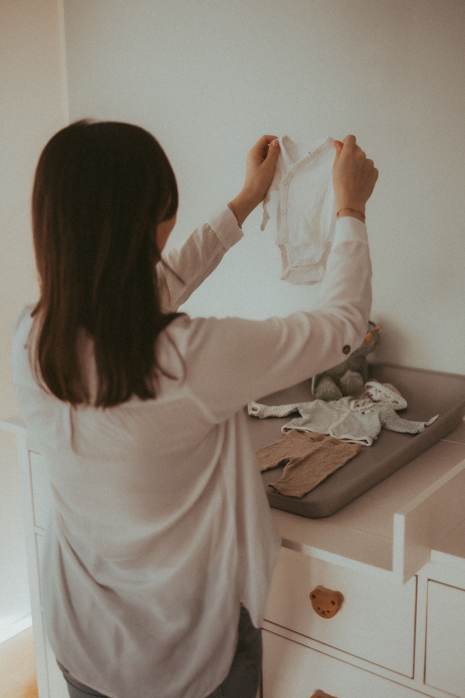 Person in white sweater arranging items on dresser in minimalist setting with muted tones.