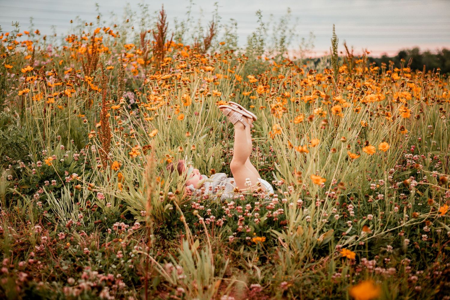 Orange wildflowers bloom in a sunny meadow with a playful maternity photoshoot pose.