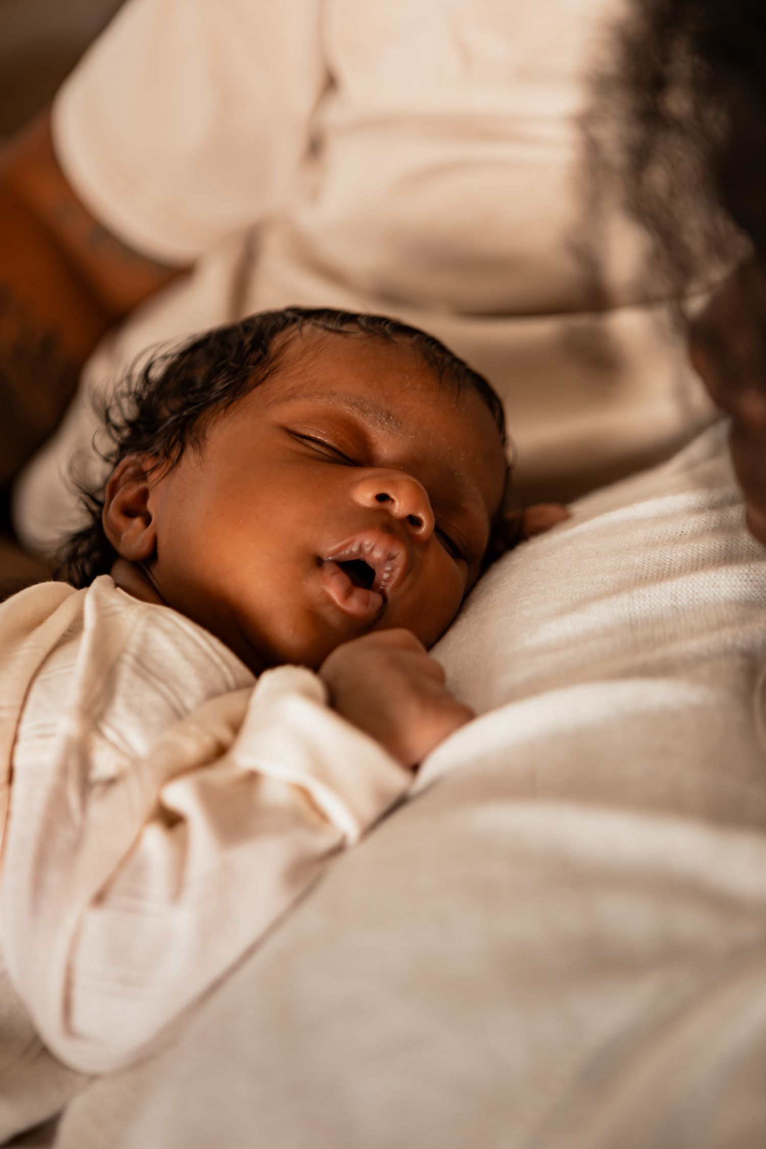 Sleeping newborn baby wearing white clothing rests peacefully on soft bedding.