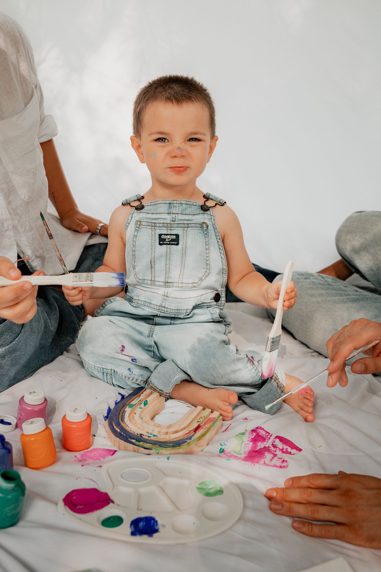 Indoor painting session showing small hands and colorful paint supplies on white backdrop.