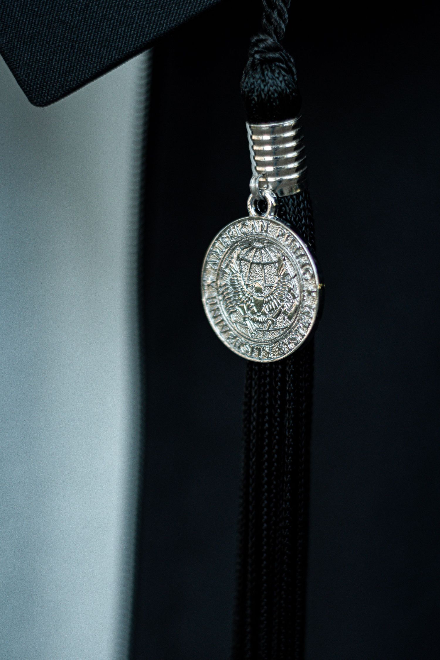 Close-up shot of a silver university medallion on black graduation tassel.