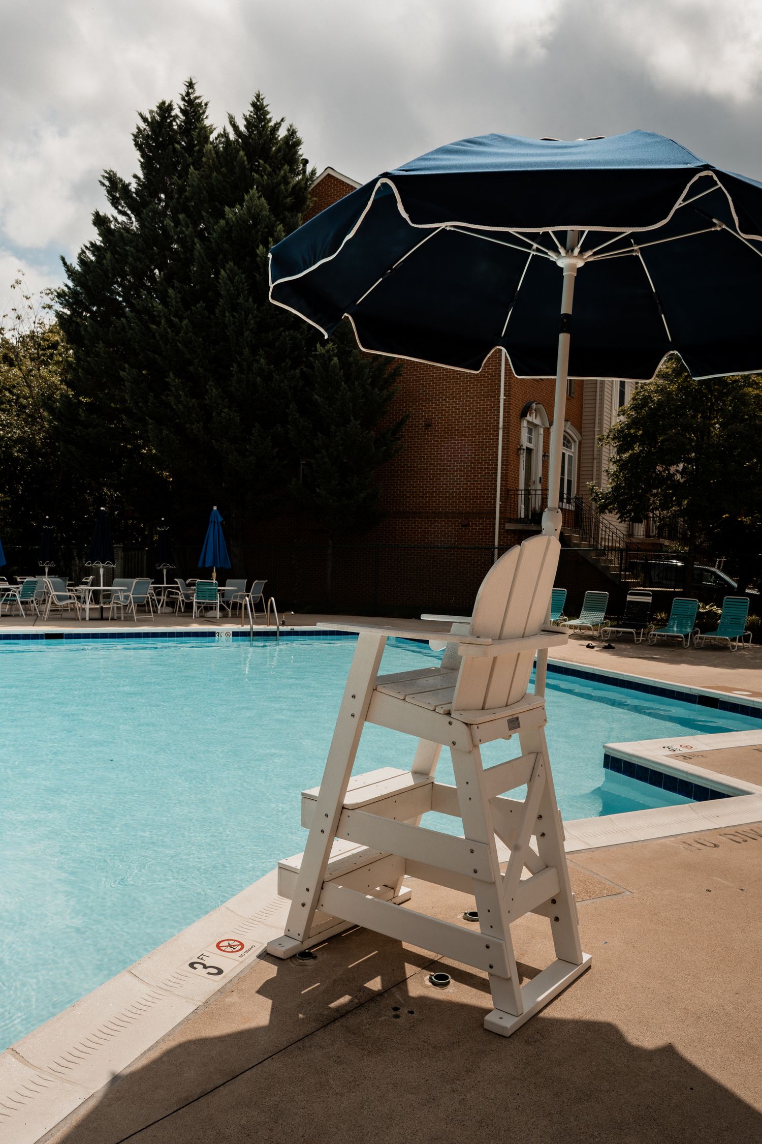 Empty white lifeguard chairs lined up along the side of a blue swimming pool.