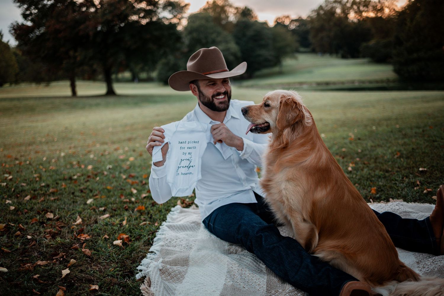 A couple sits on a blanket with their golden retriever during an outdoor photoshoot.