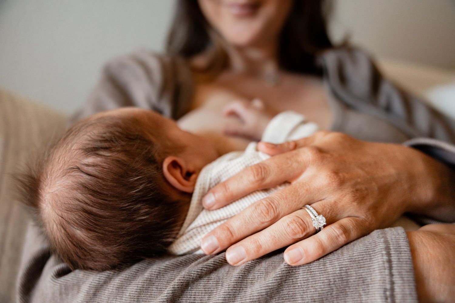 Mother breastfeeding newborn baby, close-up of infant nursing while parent gently supports with ringed hand.