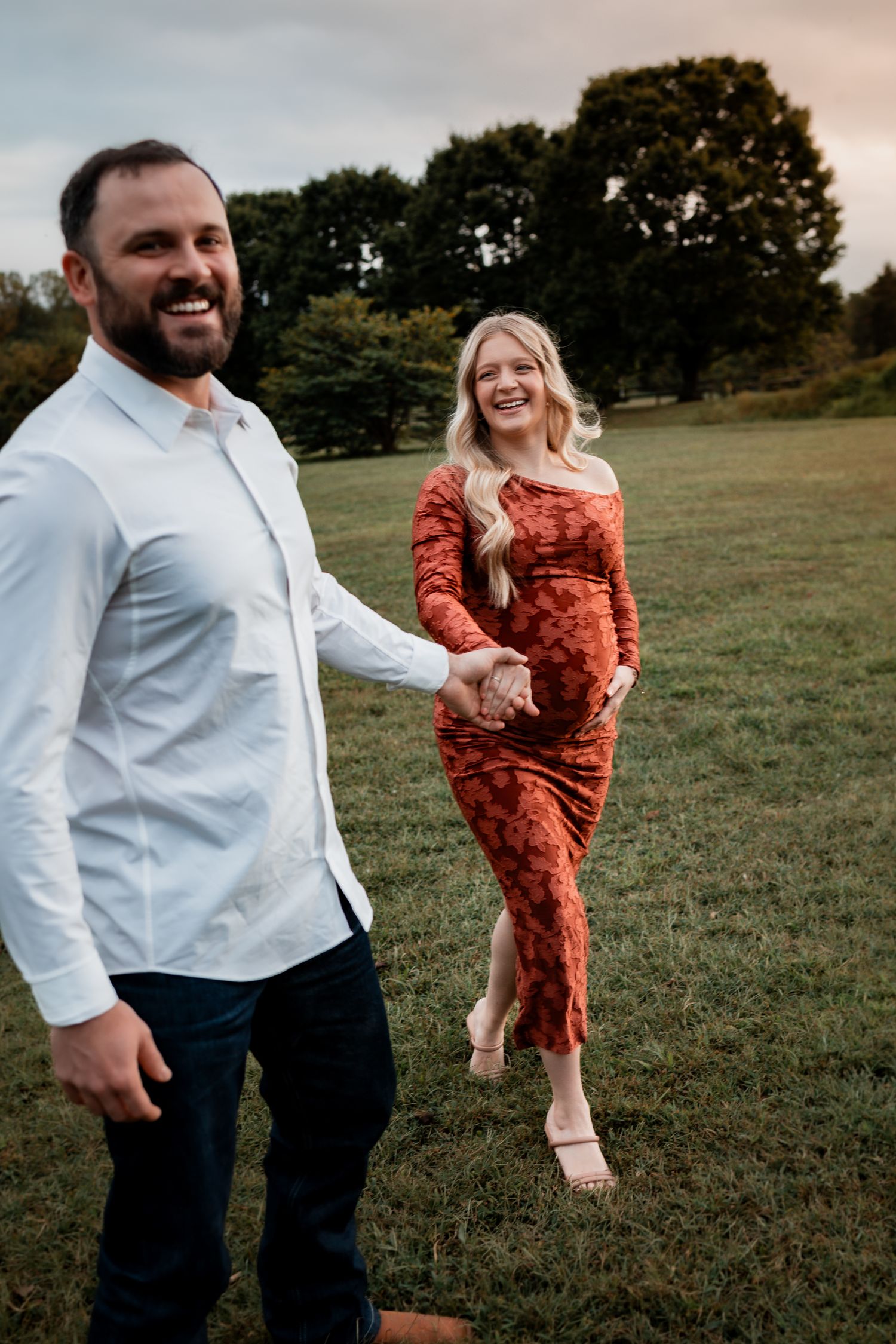 A couple dances and plays together in a grassy field during golden hour.