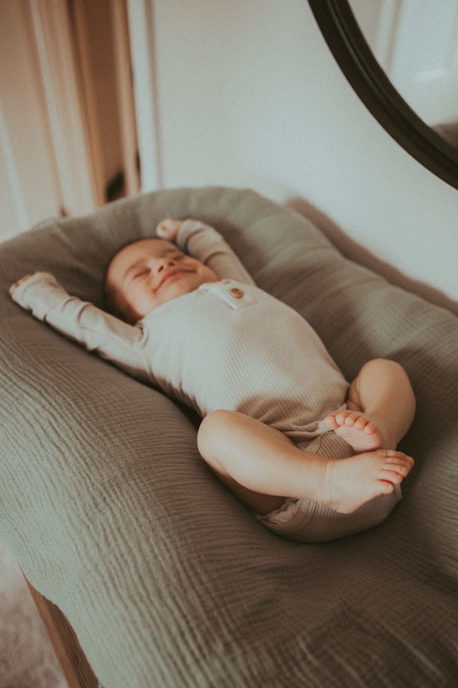 Peaceful sleeping baby in white onesie resting on textured gray bedding.