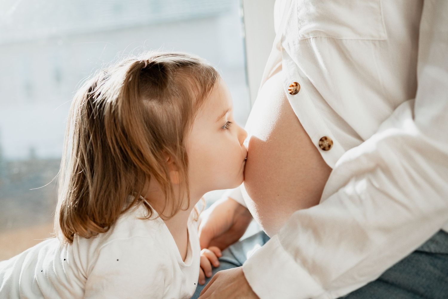 A tender moment between a young child and a pregnant belly in soft natural light.