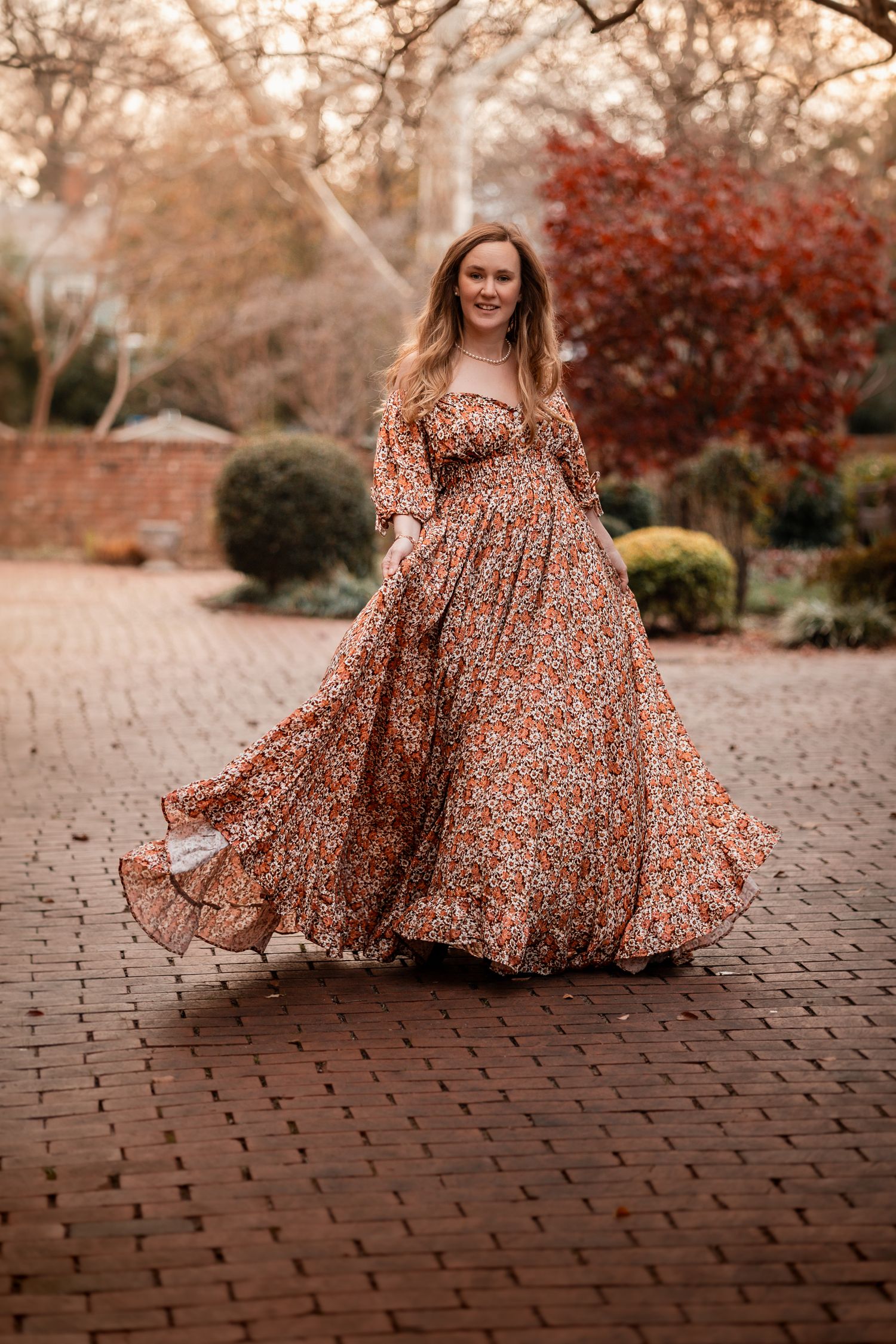 A floral dress twirls gracefully on brick pavement during an autumn photoshoot with warm golden tones.