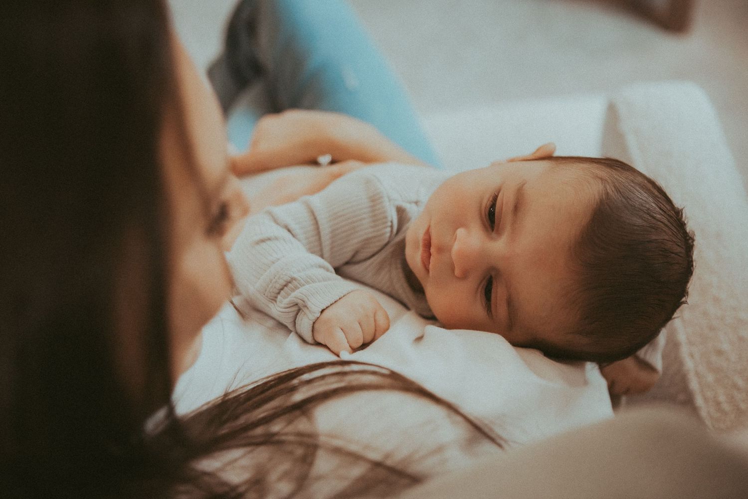 Peaceful sleeping baby wearing white onesie rests on soft white bedding in natural light.