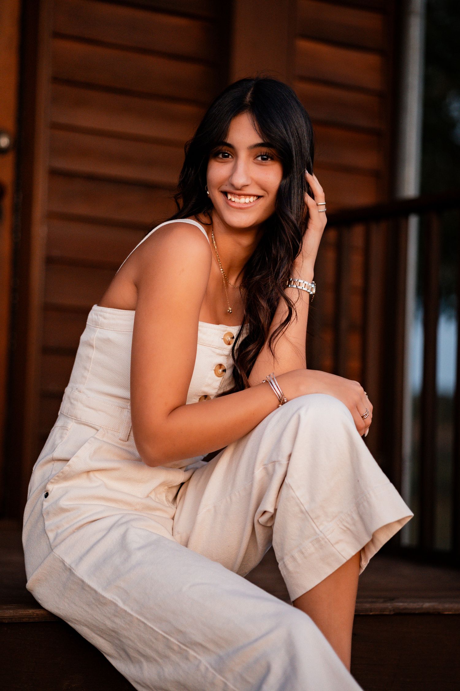 Casual outdoor portrait on wooden porch steps with stone foundation at sunset.