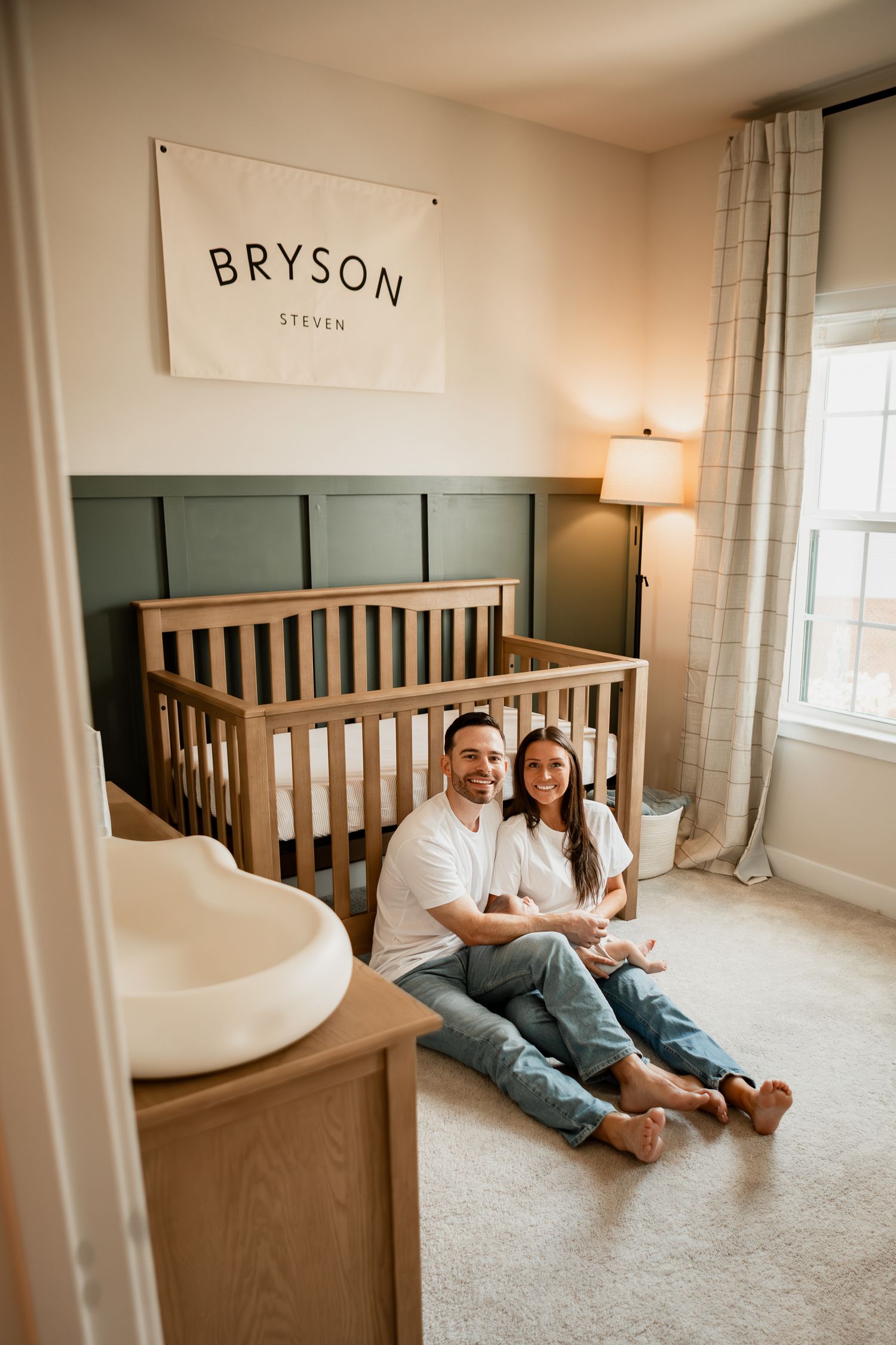 Cozy nursery corner with wooden crib and sage green accent wall featuring a name sign reading 'BRYSON' above.