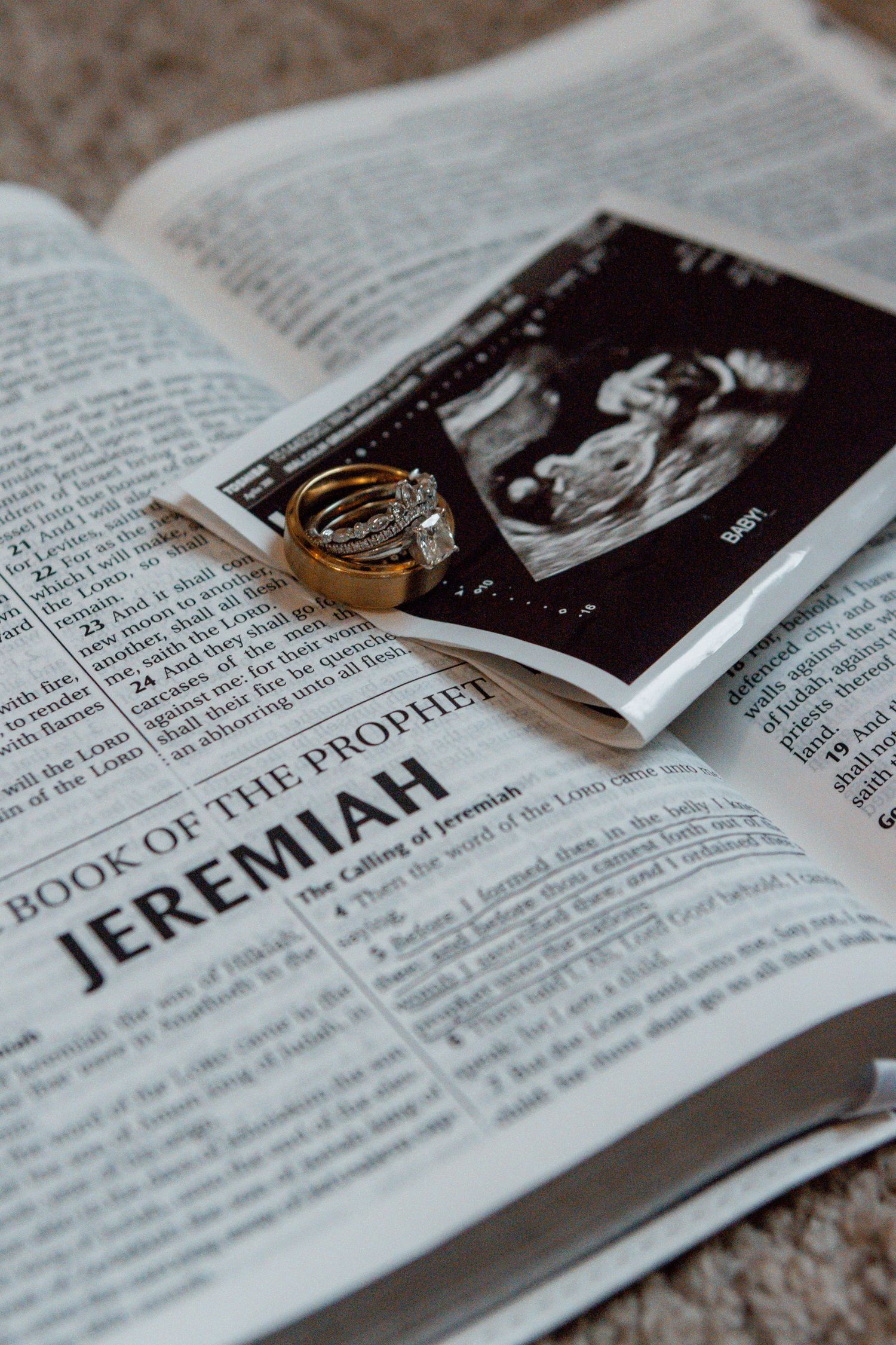Bible open to Book of Jeremiah with wedding rings and ultrasound photo placed on the pages.