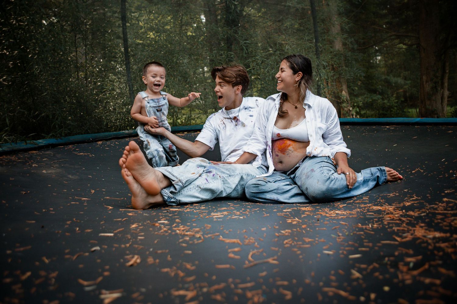 A couple lies together laughing among scattered autumn leaves on a paved outdoor surface.