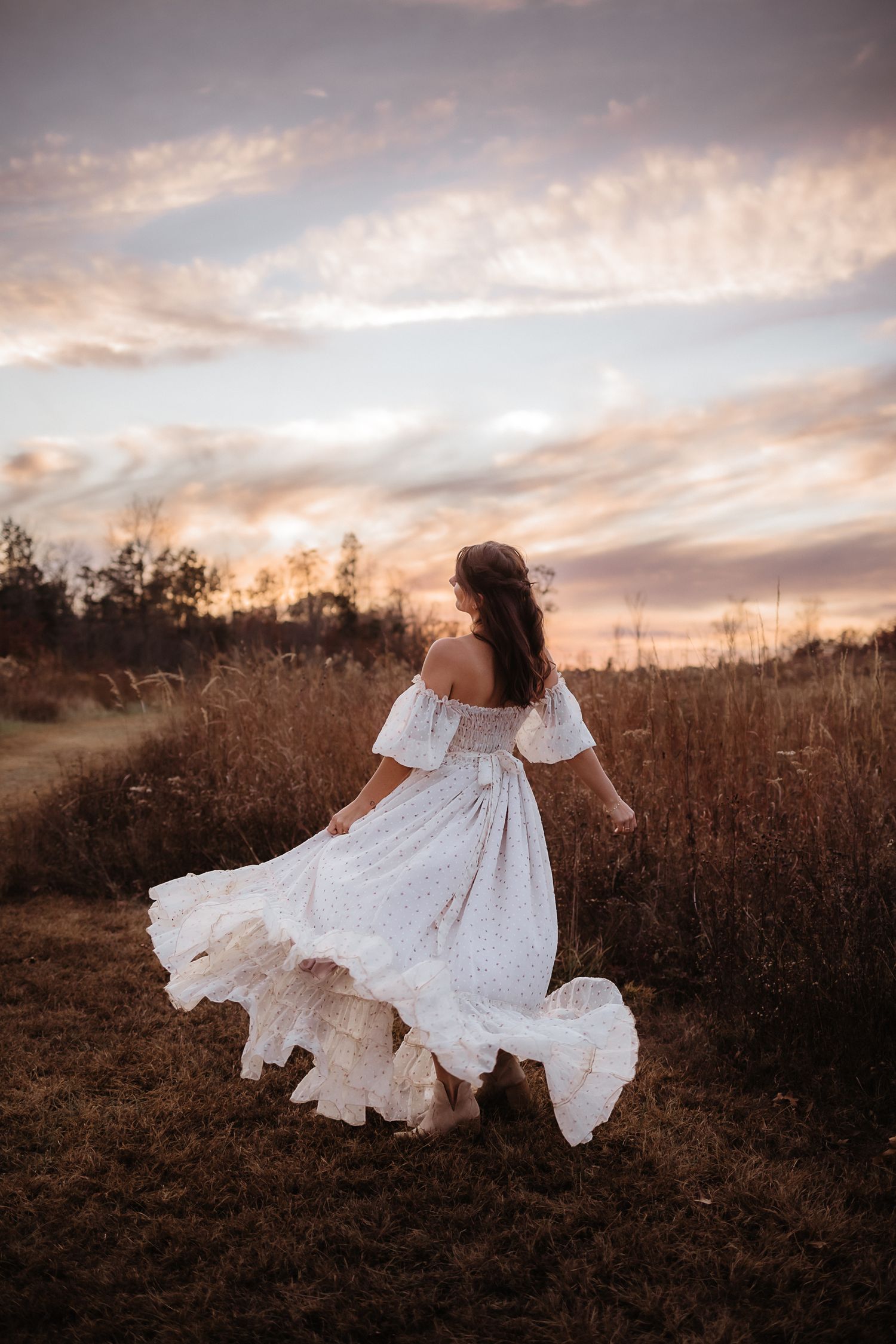 A figure in a flowing white dress twirls gracefully in a golden field at sunset.