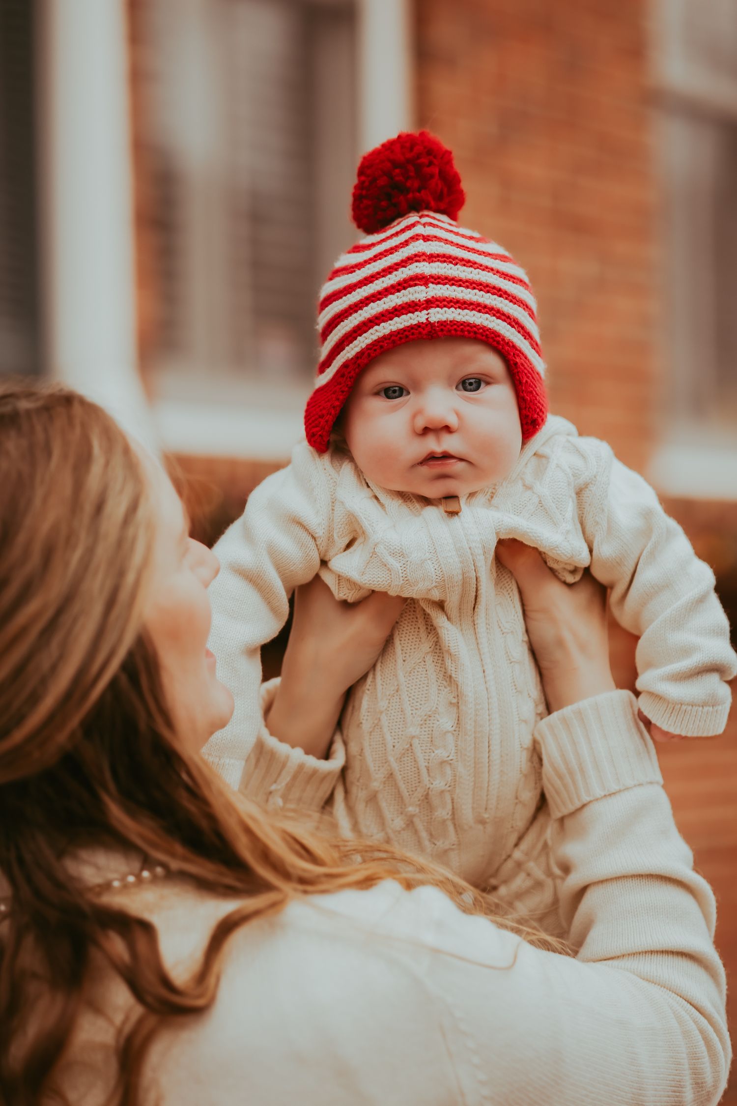 A baby wearing a red striped winter hat and white outfit is held up during a family photo session.