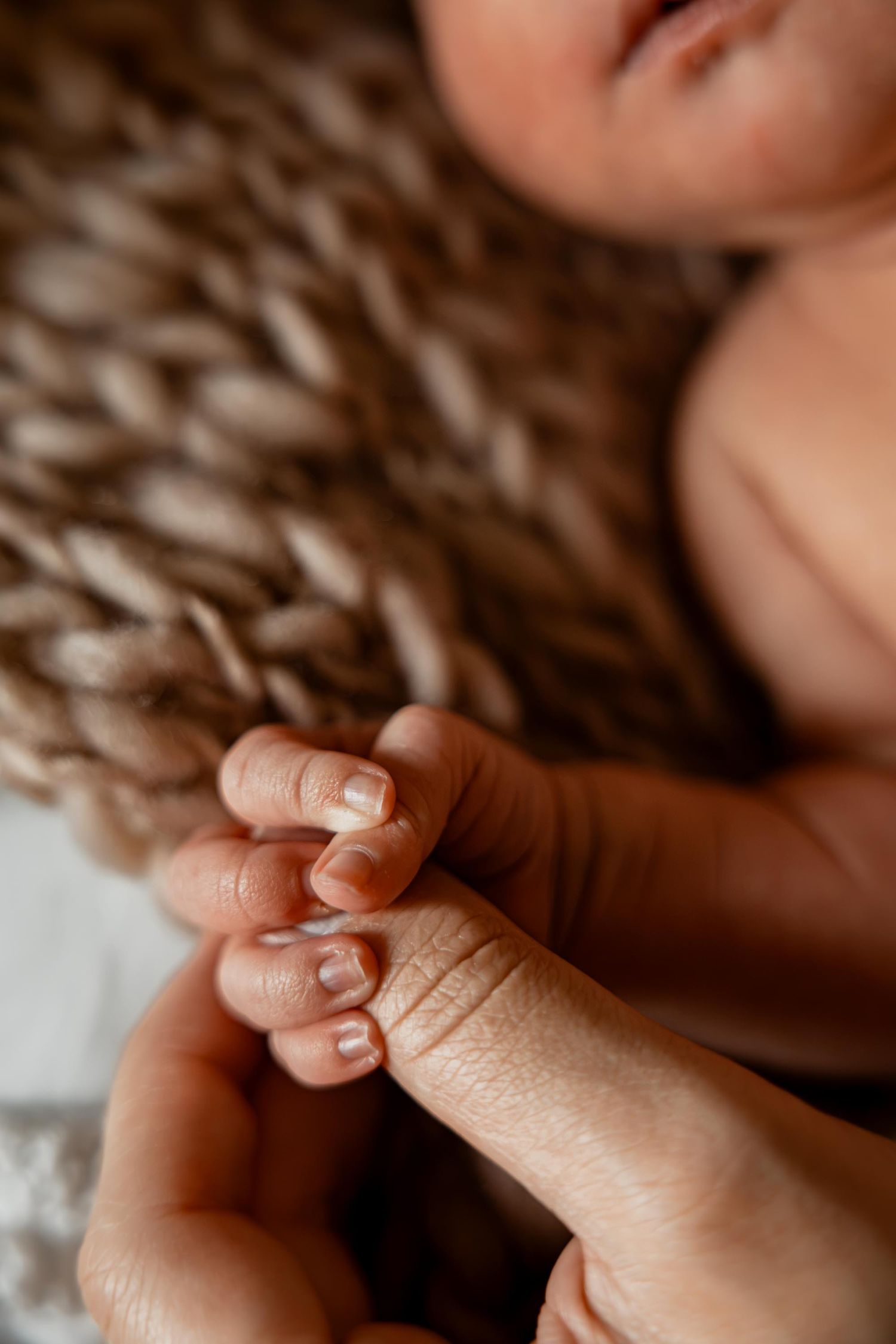 Close-up of a newborn baby grasping an adult finger, showing tiny delicate hands and nails.