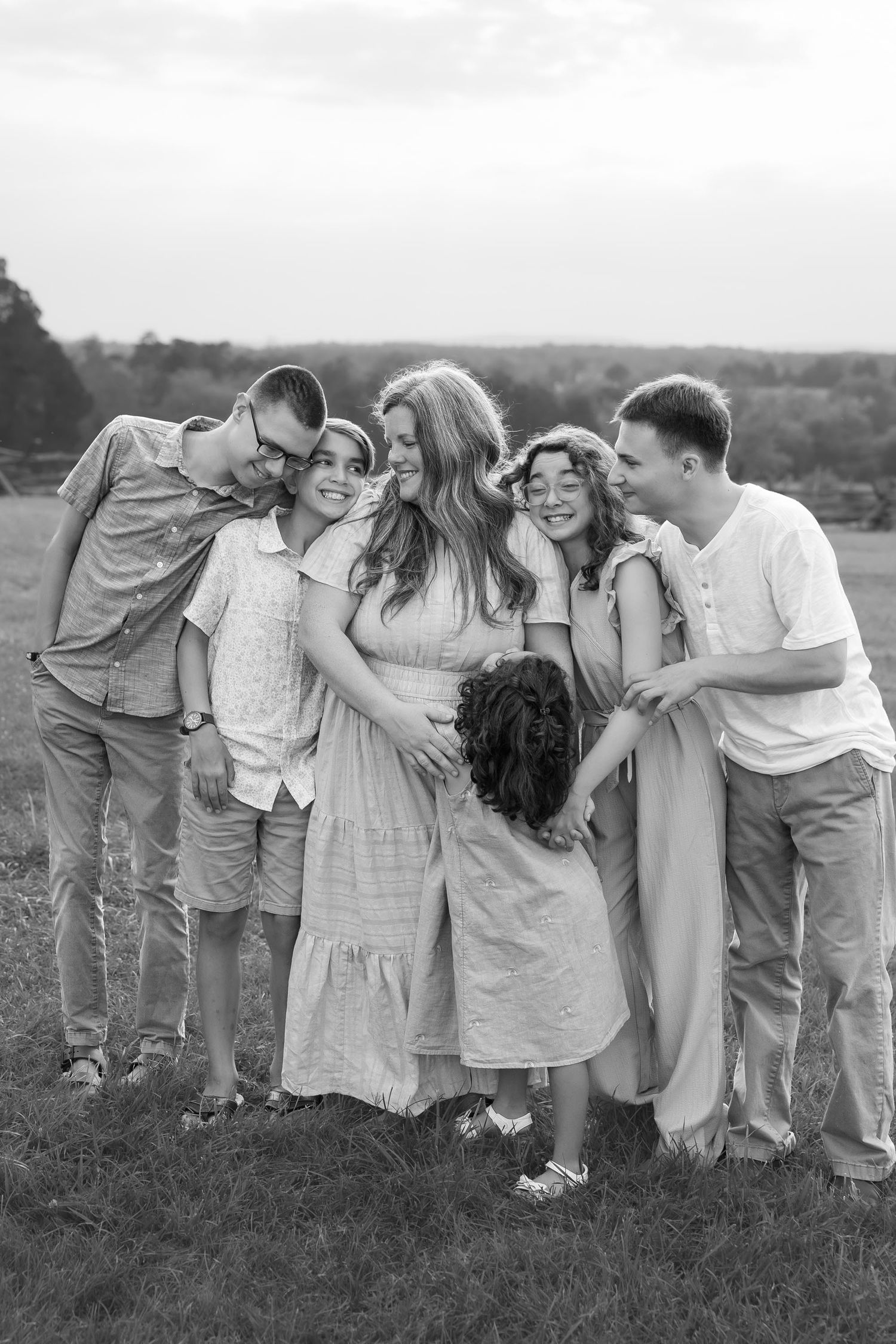 A joyful blended family shares a warm group hug in a grassy field during an outdoor photo session.