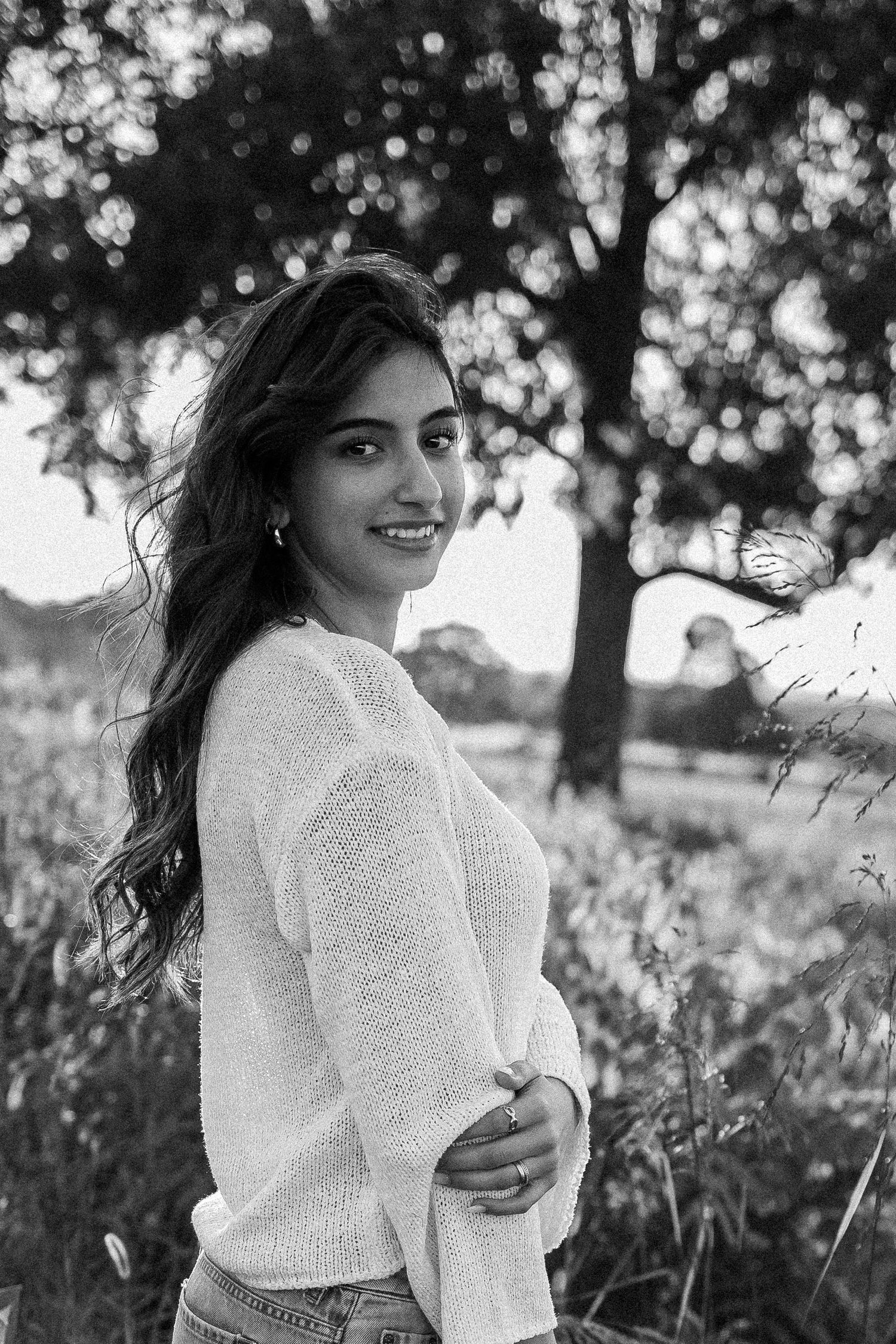 Black and white outdoor portrait of someone wearing a white sweater among trees in natural light.