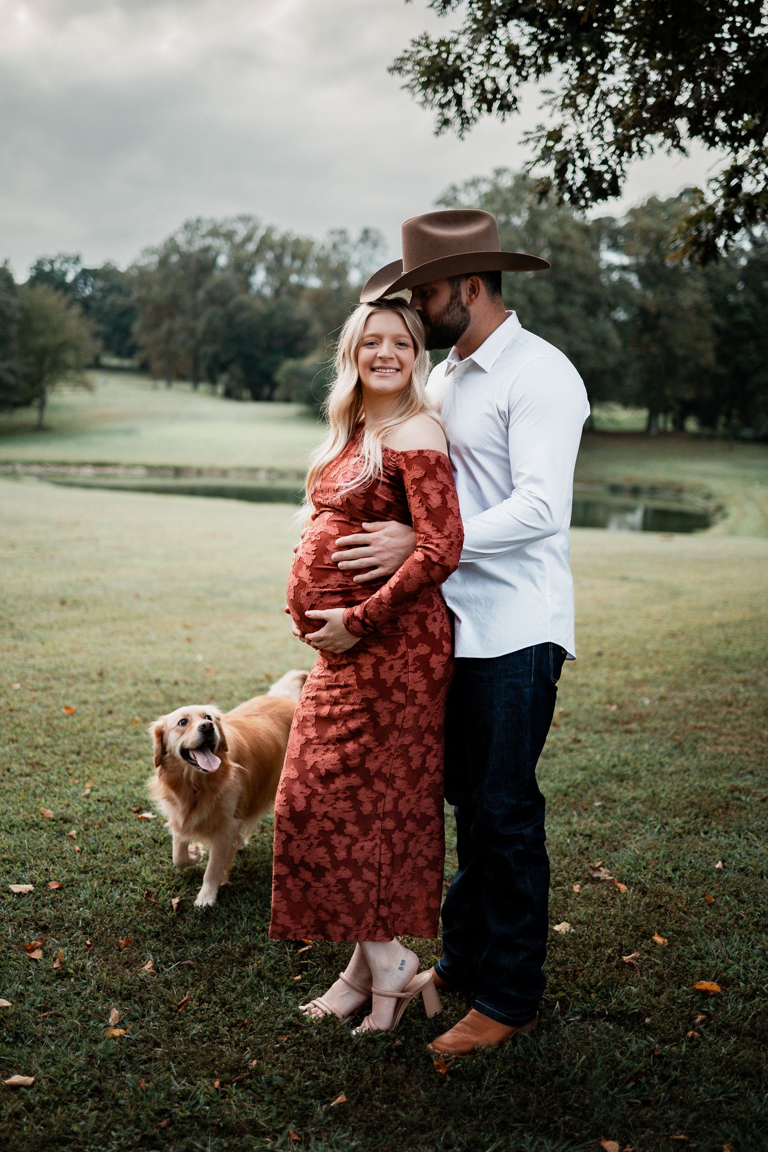 Maternity photo session in a park with a golden retriever joining the couple.