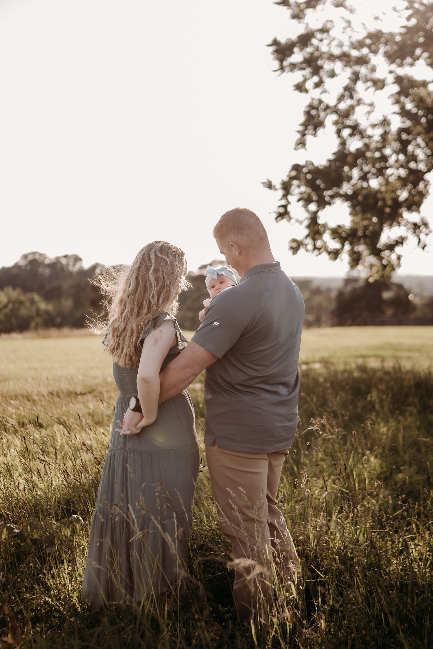 A romantic moment captured in golden hour light as two people stand together in tall grass.