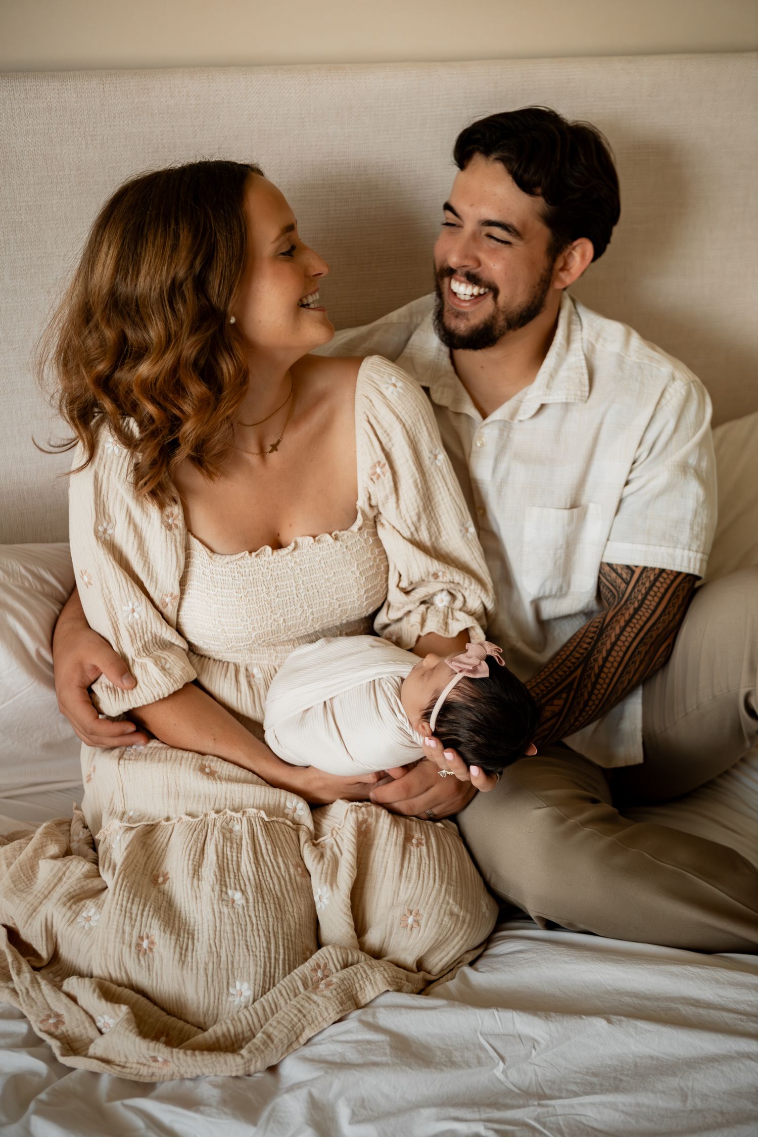 Intimate couple in white clothing embracing and smiling together on light colored bedding.