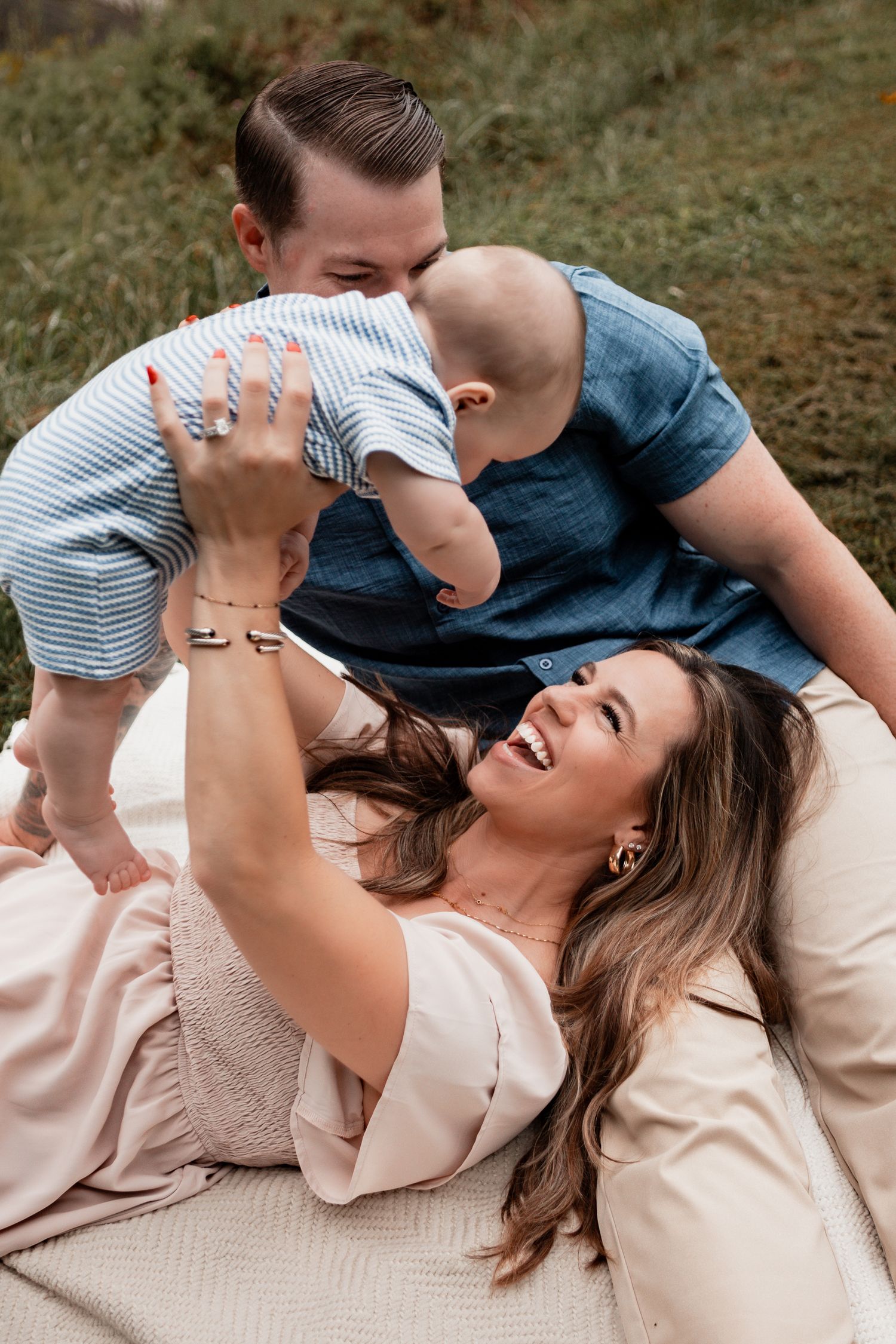 Family lying on blanket outdoors sharing joyful playful moments together on sunny day.