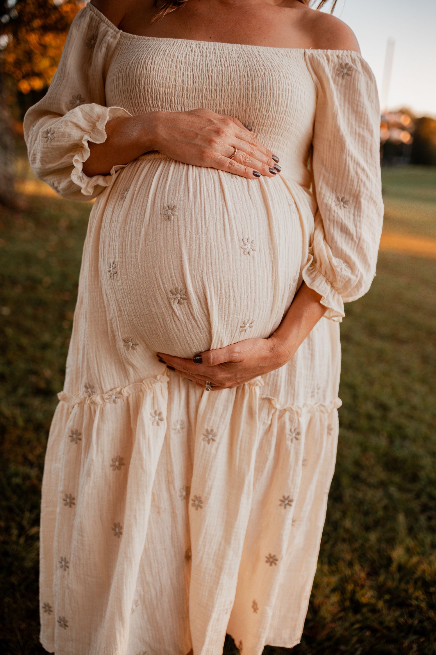 Close-up shots of a pregnant belly in a flowing white embroidered dress against a sunset-lit outdoor setting.