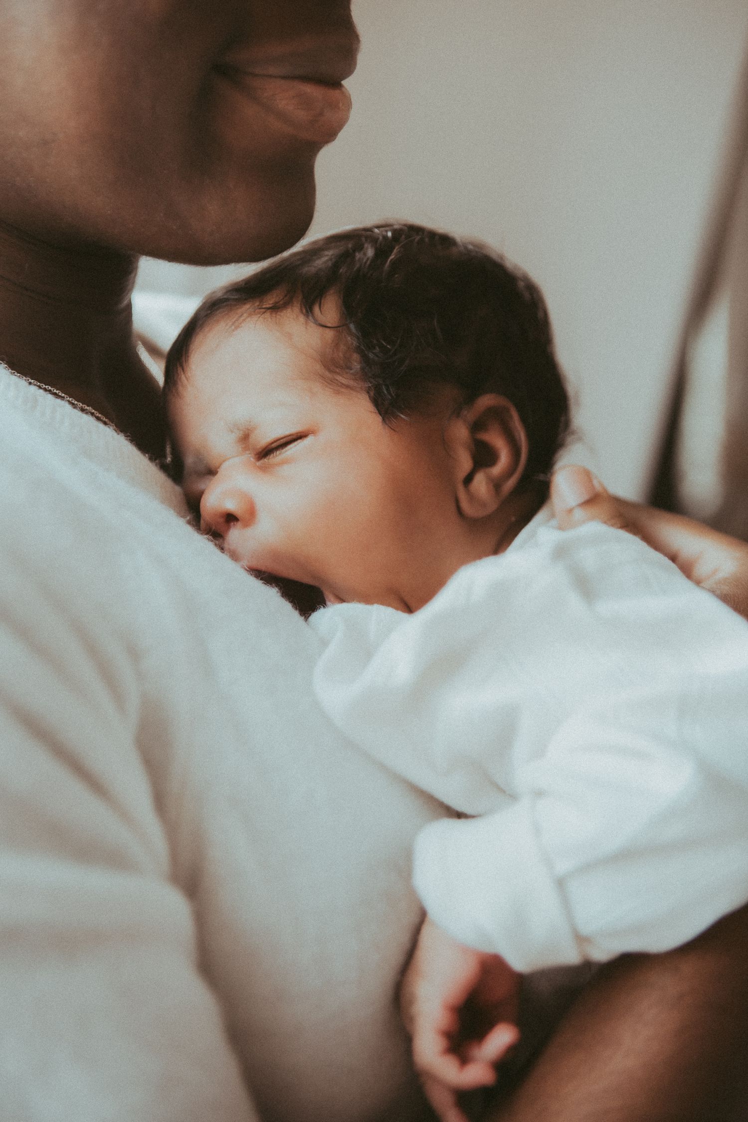 Peaceful sleeping newborn baby swaddled in white blanket with soft natural light.