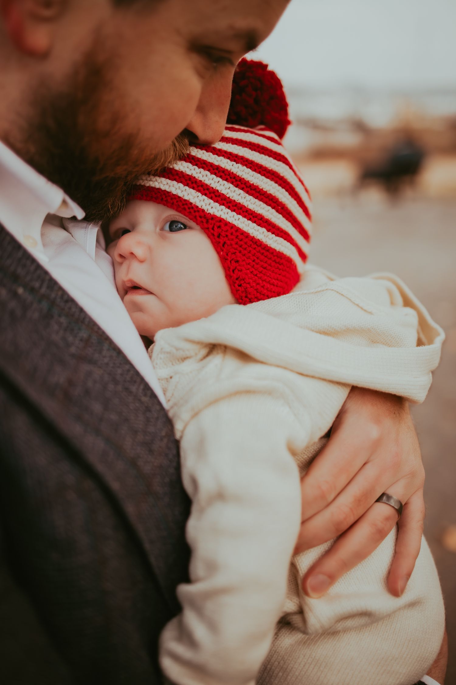 Close-up shots of a baby wearing a red and white striped winter hat and white outfit being held tenderly.