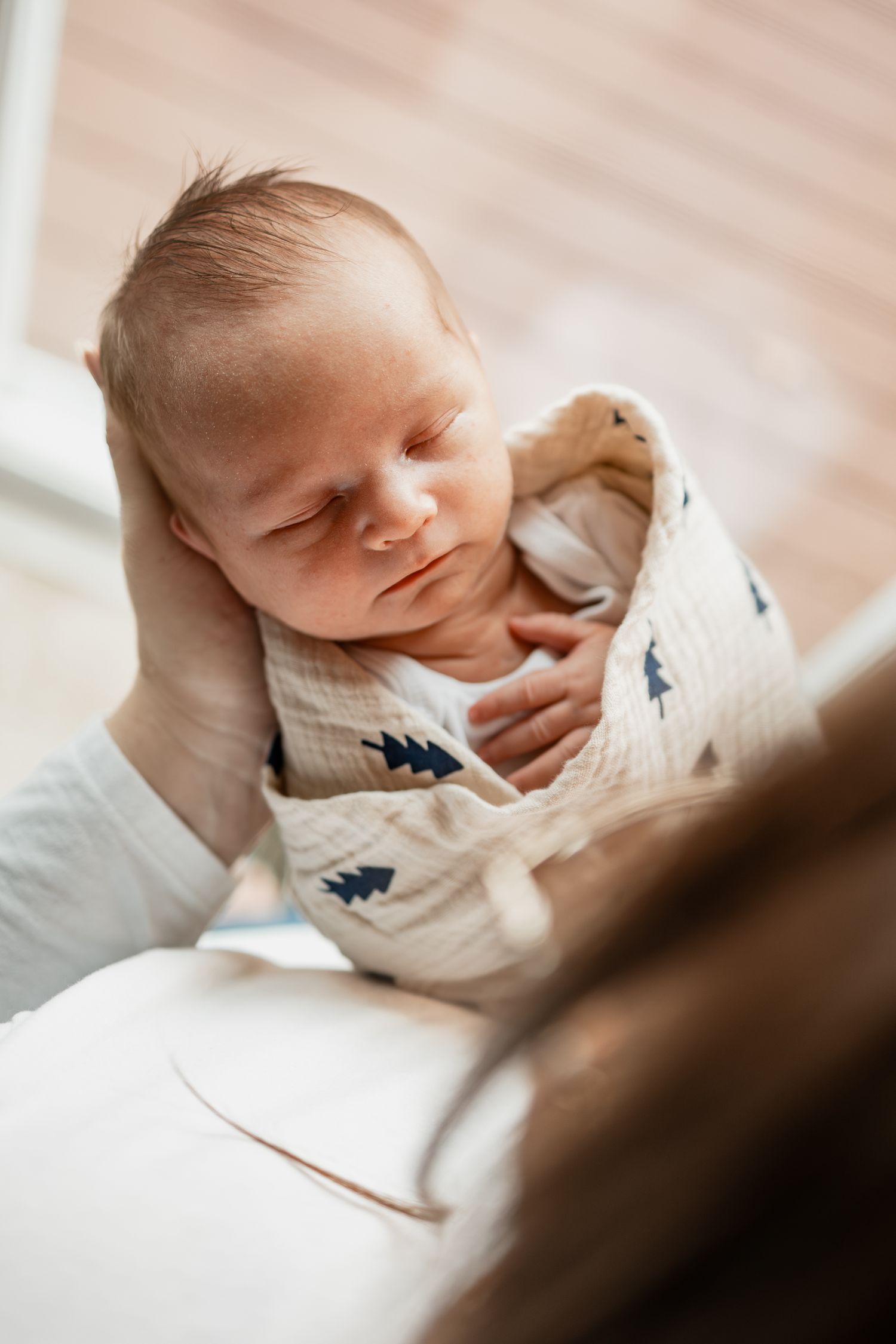 A sleeping newborn baby wearing a white onesie with blue details is captured in a series of close-up shots.