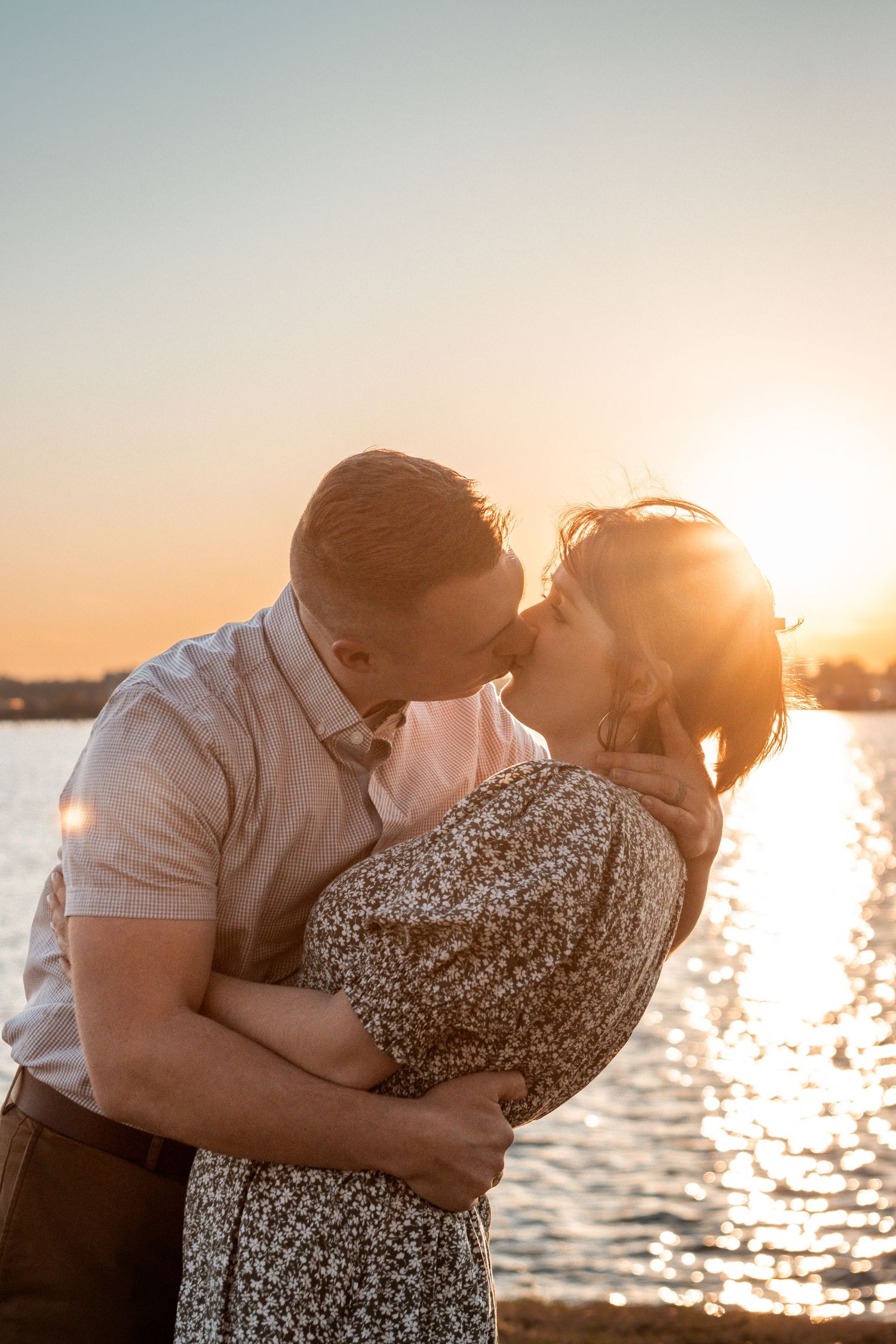 A romantic couple sharing an intimate moment at sunset by the waterfront.