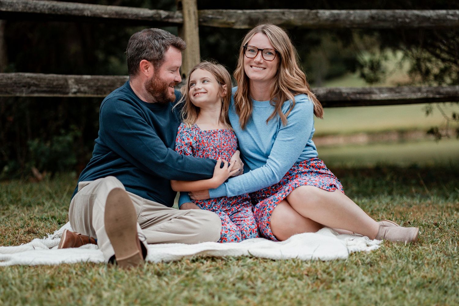 A couple sits together on a blanket in a grassy outdoor setting during a romantic photoshoot session.