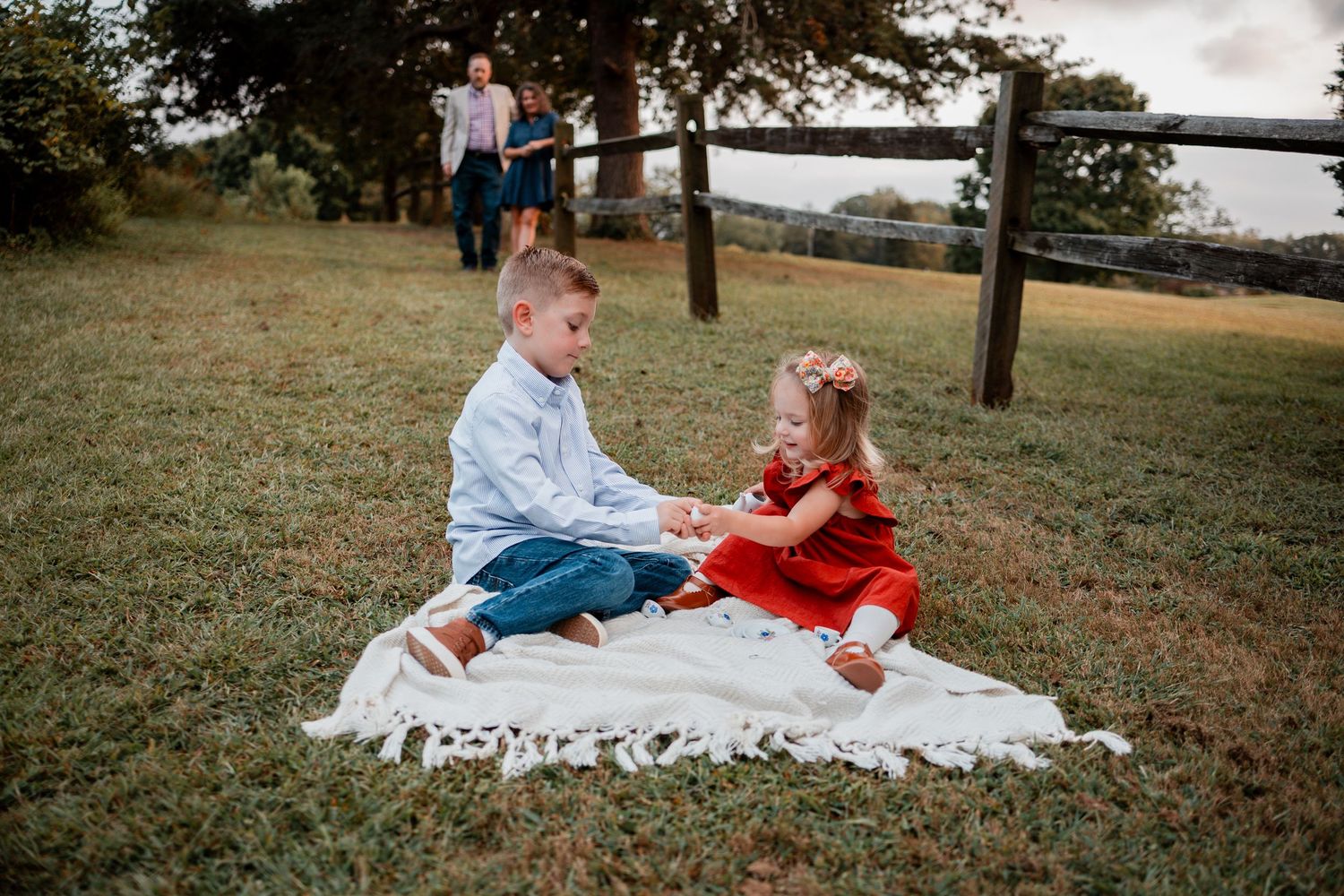 Two people share a picnic on a white blanket in a grassy field during sunset.