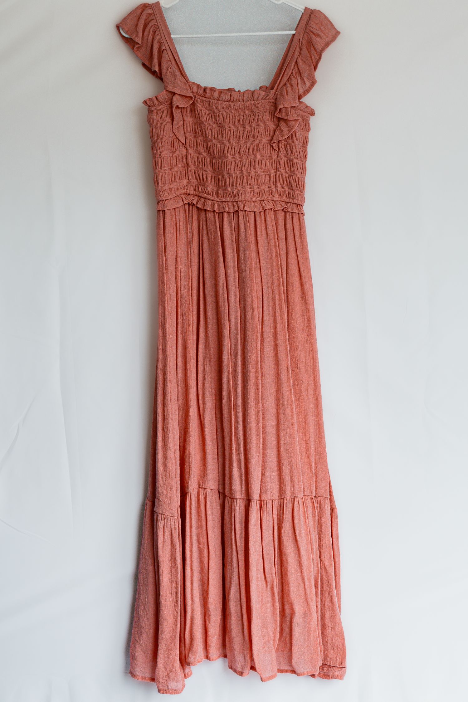 A coral-colored maxi dress with smocked bodice, ruffle cap sleeves and tiered skirt hangs on a white hanger.