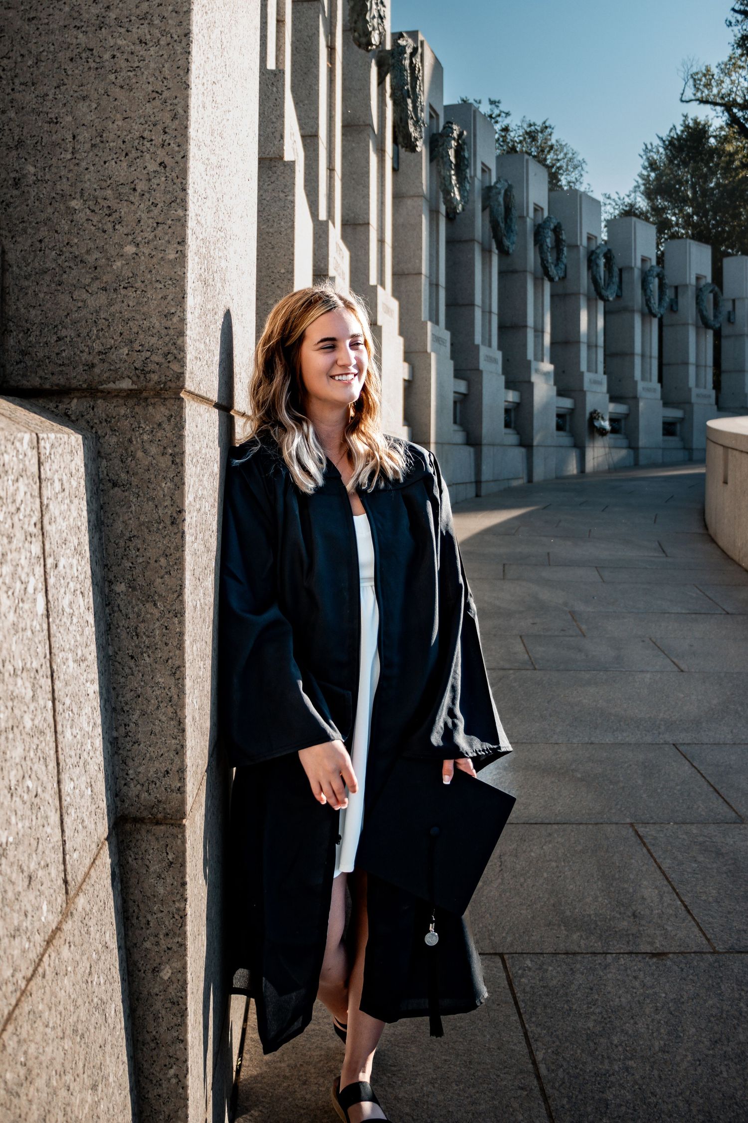 Professional graduation photos taken against a row of classical stone columns and pillars in an outdoor setting.