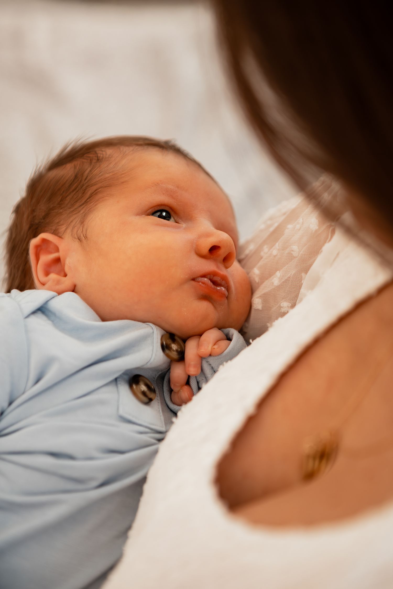 A newborn baby in a light blue outfit nursing while being cradled.