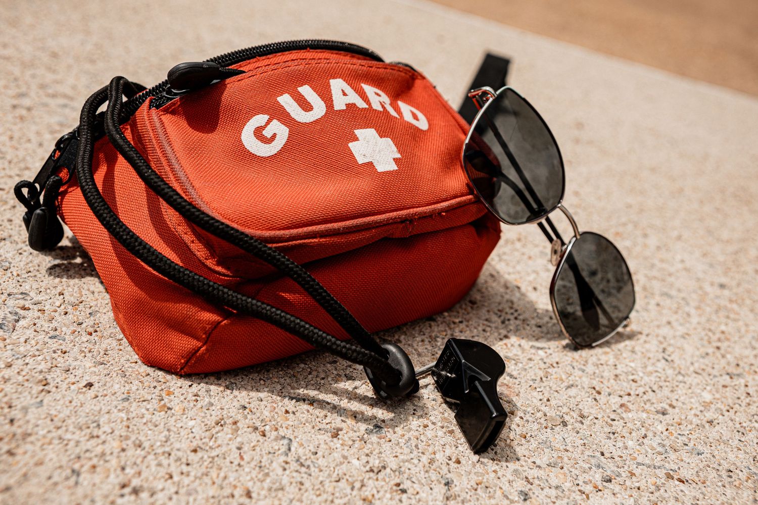 Red lifeguard medical bag with sunglasses on sandy surface.