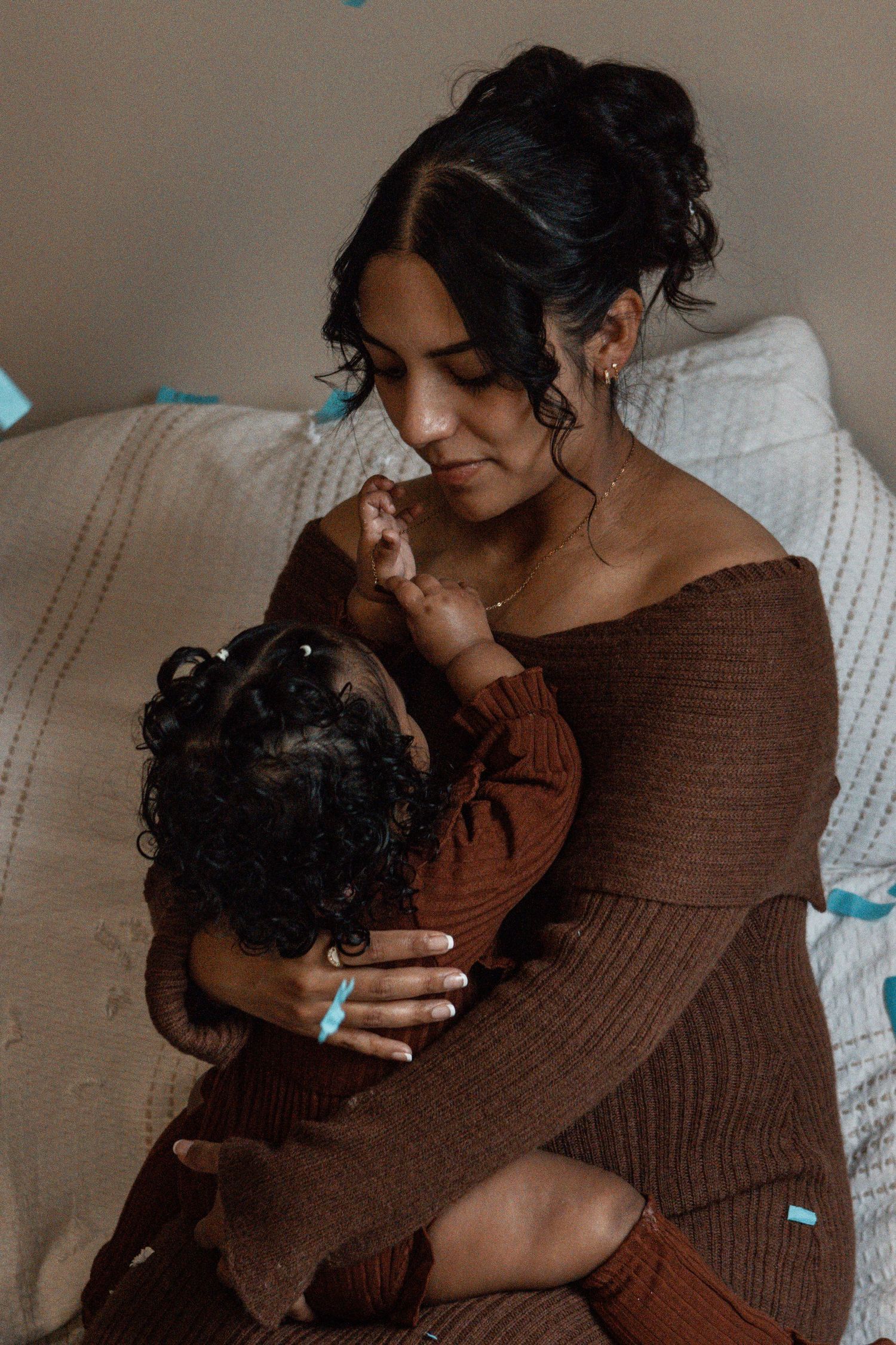 A tender moment between parent and infant wearing matching brown outfits while sitting on a cozy couch.