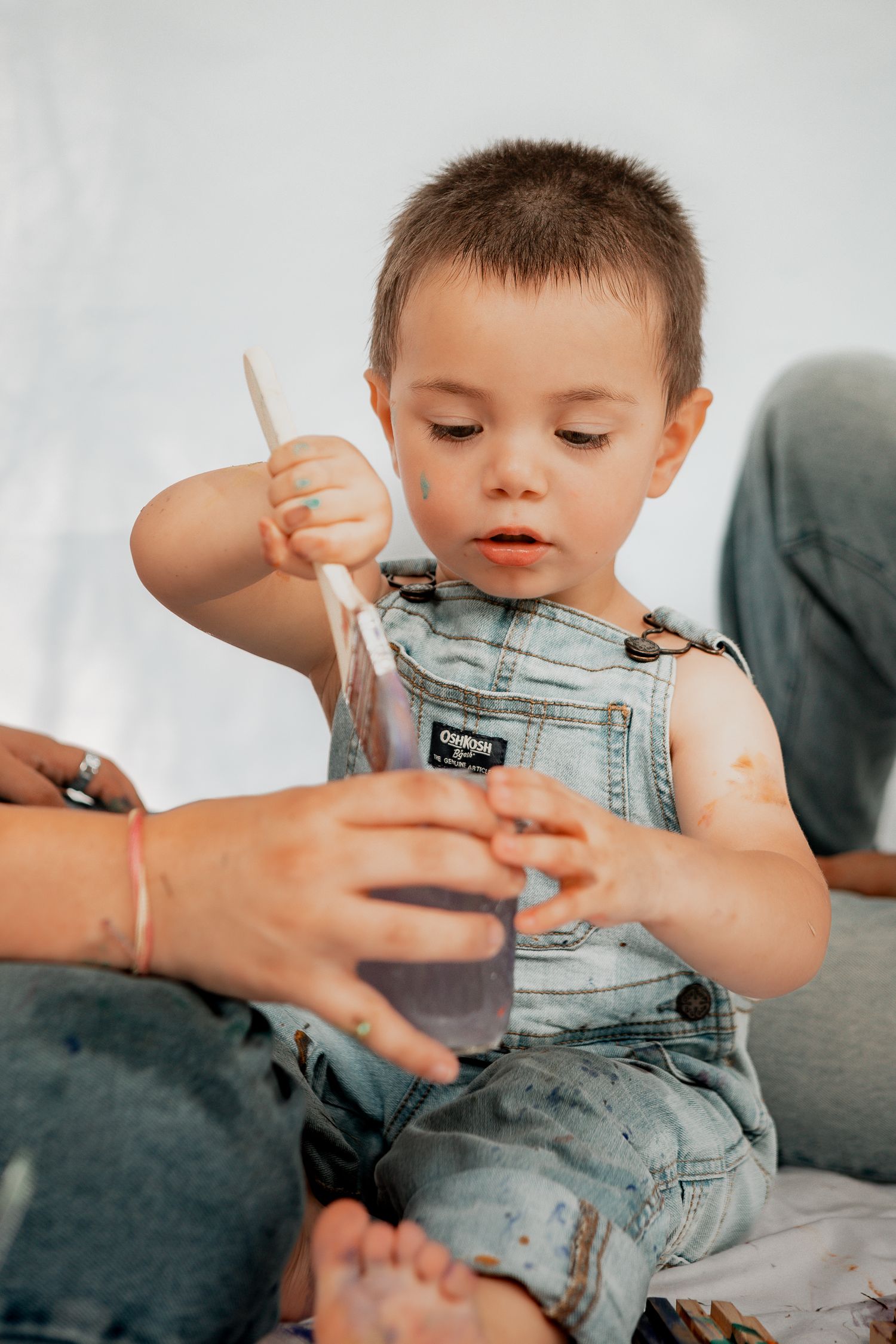 Close-up series of a toddler wearing denim overalls sitting on a couch while playing with someone's hands.