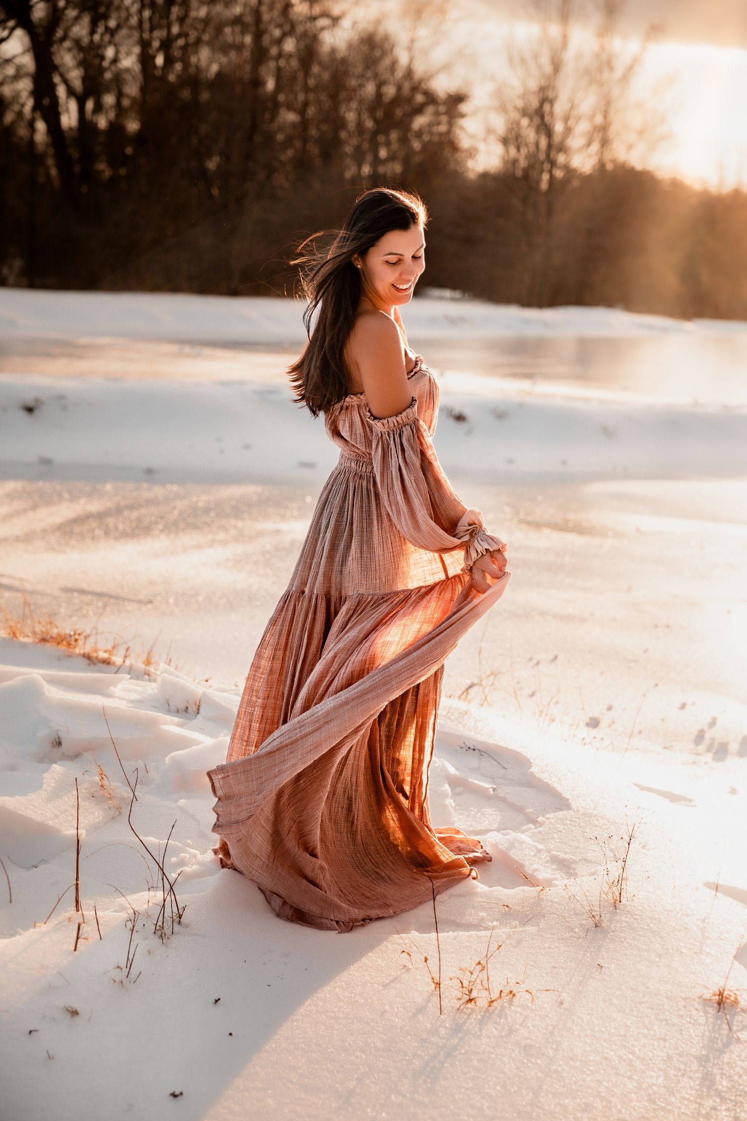 Woman in flowing pink dress twirling in snowy landscape at golden sunset hour.