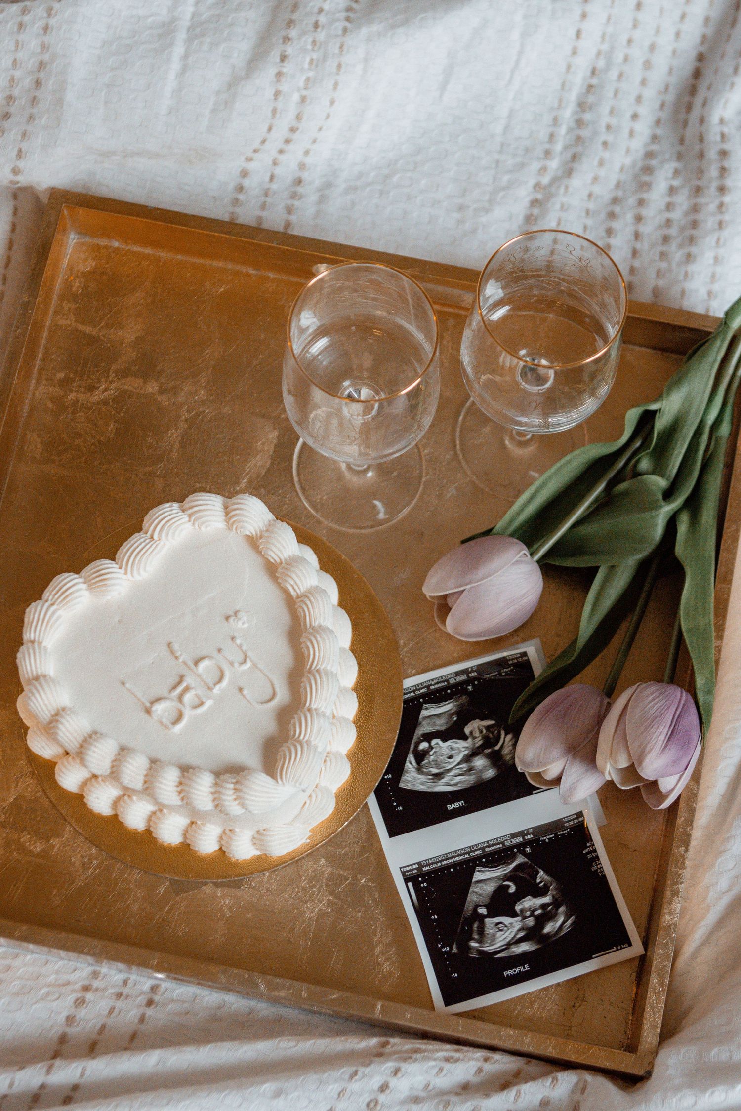 Baby announcement setup with heart-shaped cake, ultrasound photos, wine glasses and pink tulips
Gender reveal session 
Milestone Photography