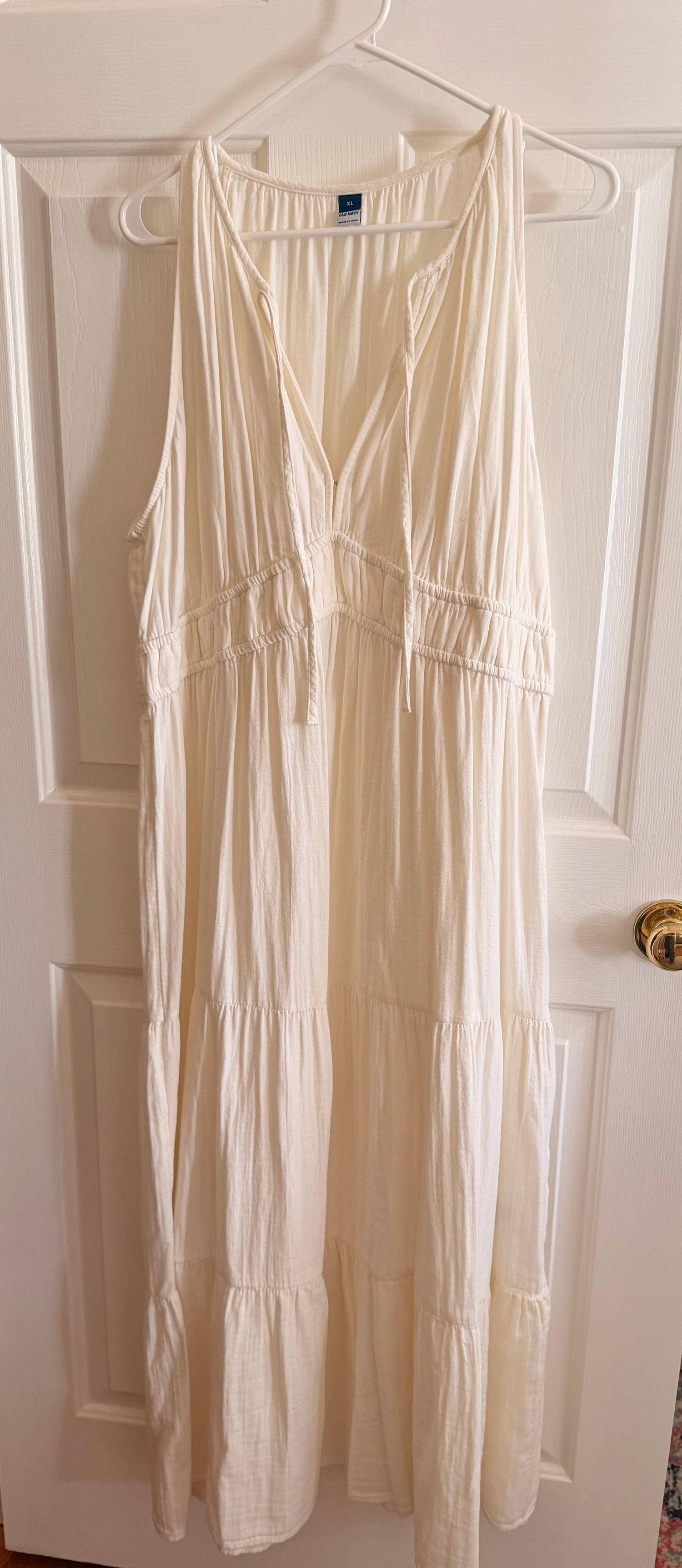 Cream sleeveless tiered maxi dress with V-neck and ruched details, hanging on a white door hanger.