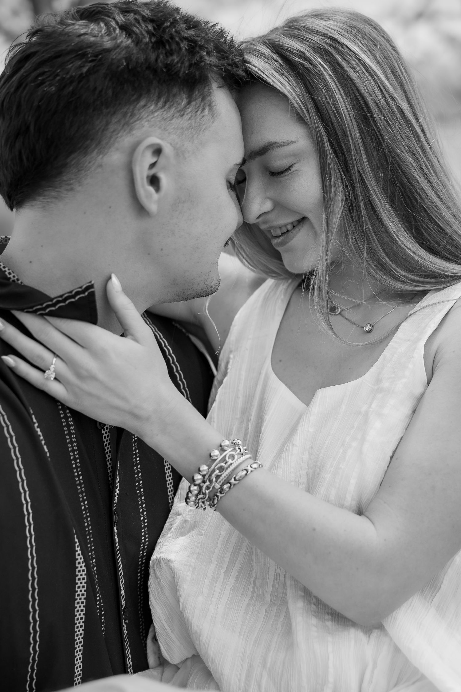 Black and white photo of a smiling couple embracing closely, woman wearing bracelets and ring, man in striped shirt.