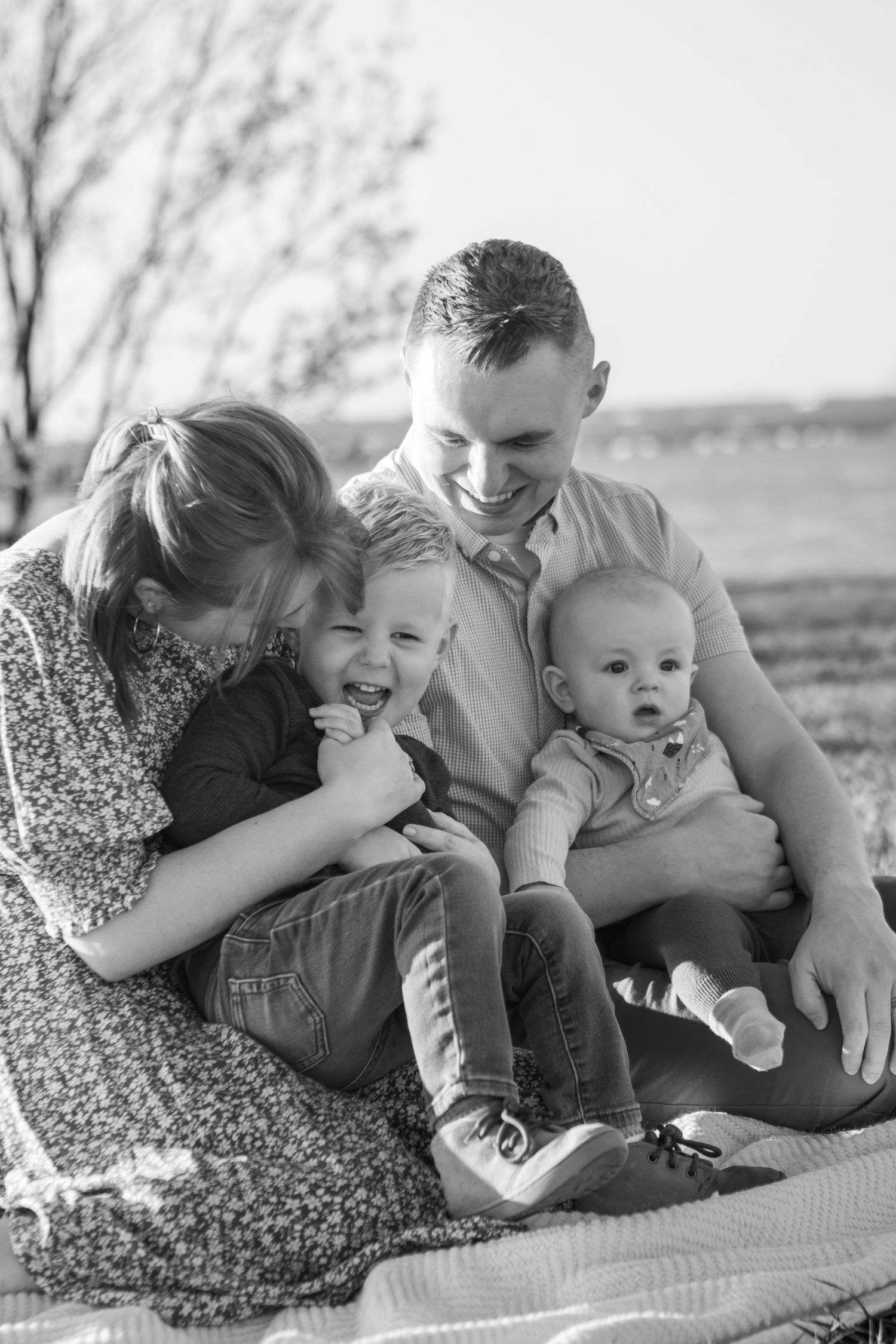 A joyful family candid moment captured in black and white as they sit together outdoors on a blanket.
